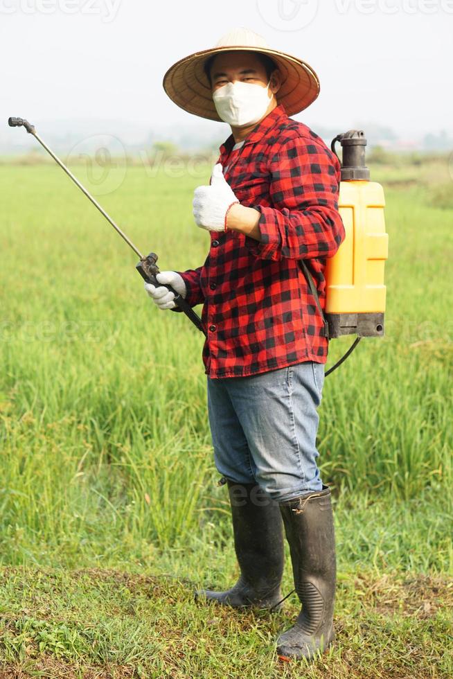 Handsome Asian farmer is spraying organic fertilizer at paddy field. Concept using friendly product with environment , Agriculture with no chemicals using. Safety with user and environment. photo