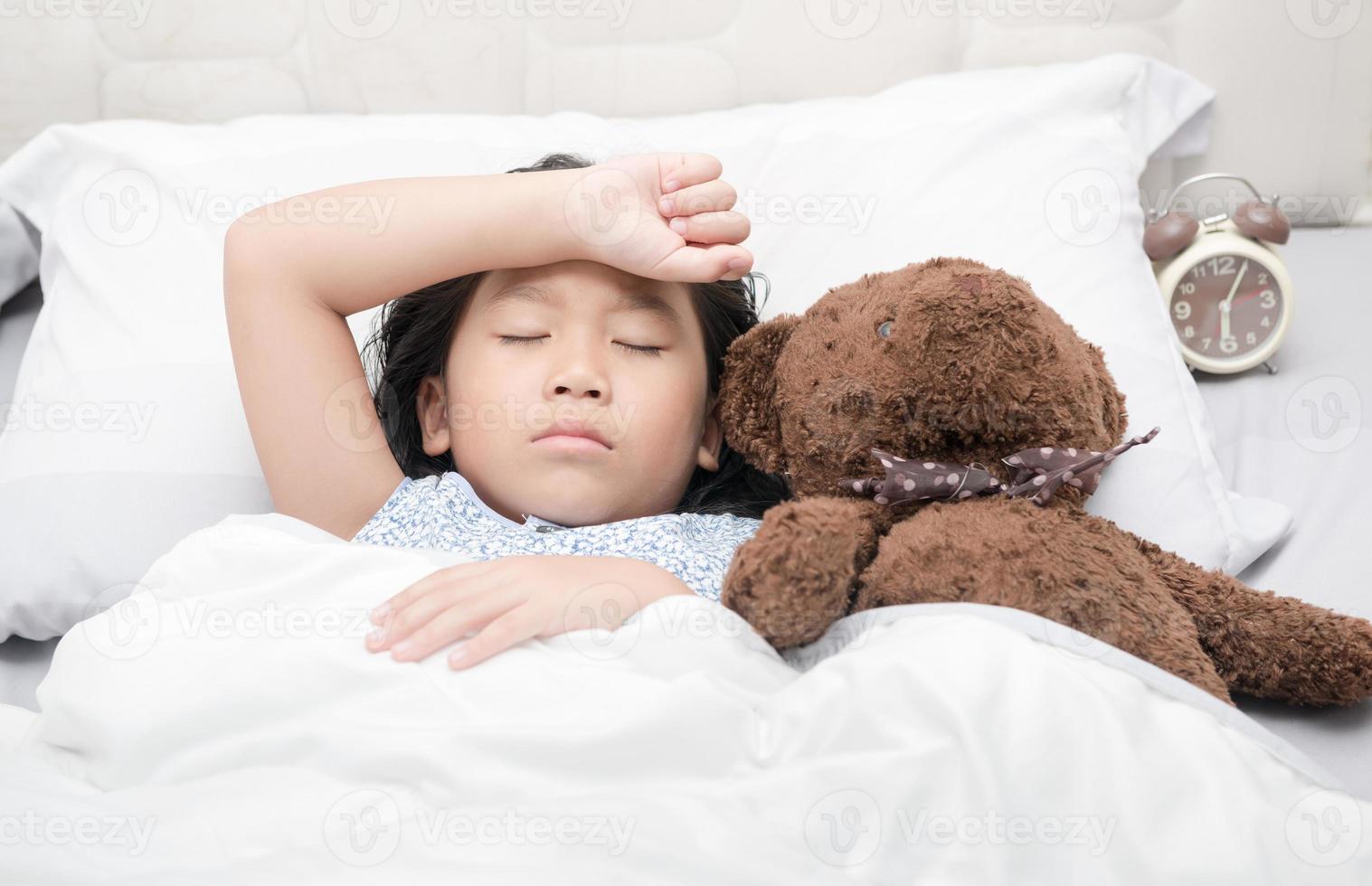 kid girl sleeping and sick on the bed with bear doll photo