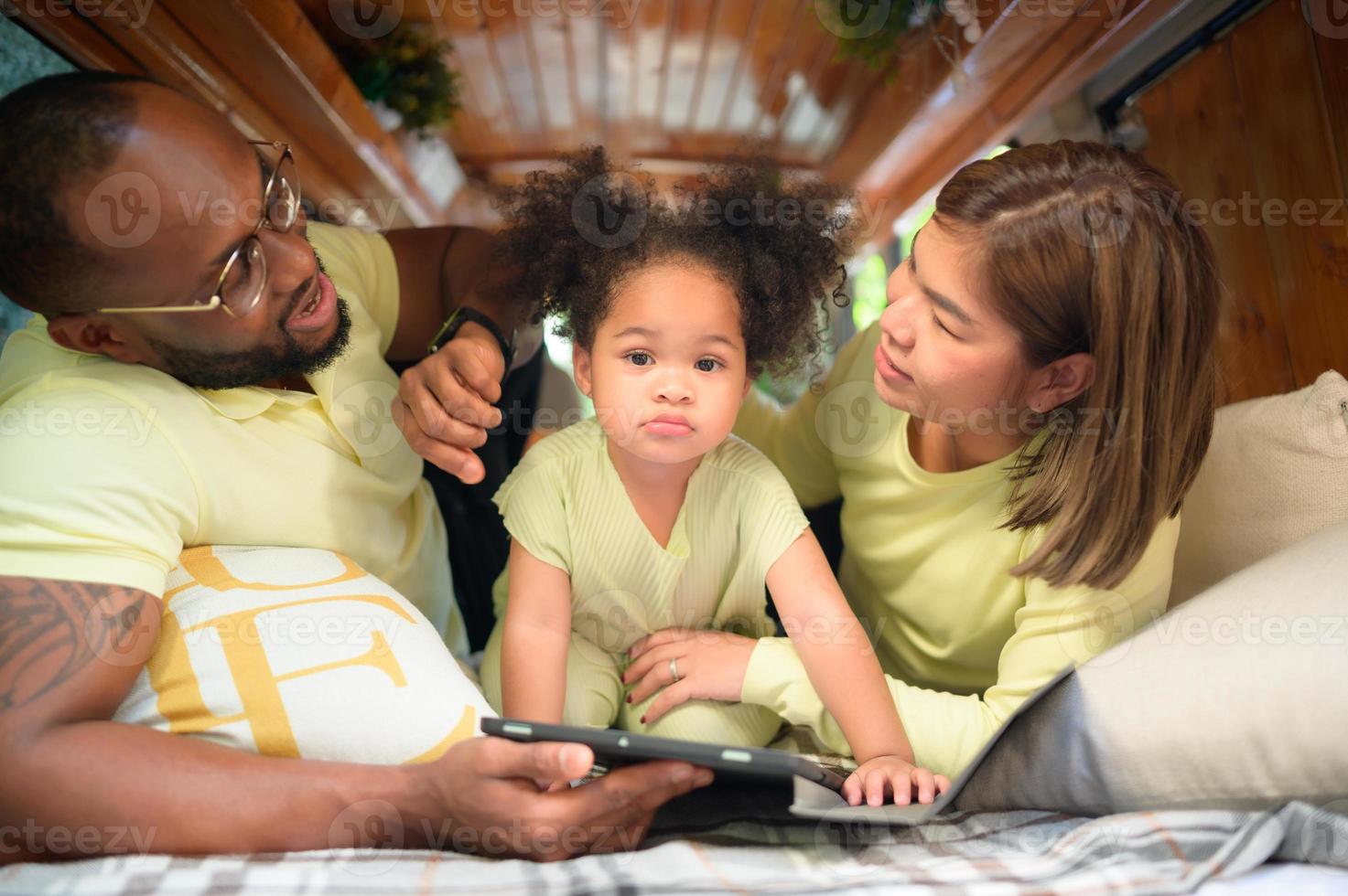 The back of a white classic van, little kids play and learn about the world on their tablet with parents taking care of helping. photo