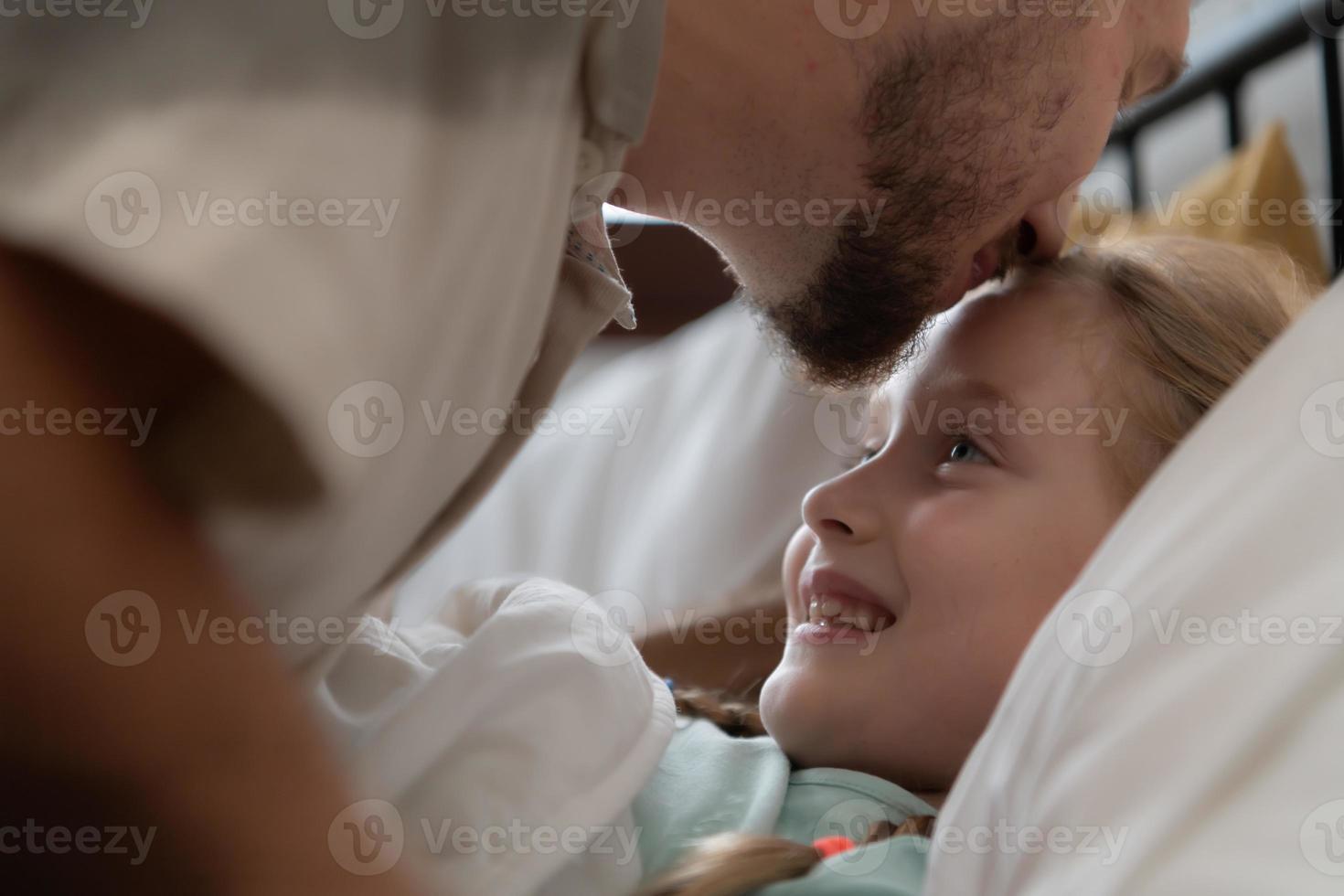 Before retiring to night, a father expresses his affection by kissing his daughter on the forehead. to get a good night's rest photo