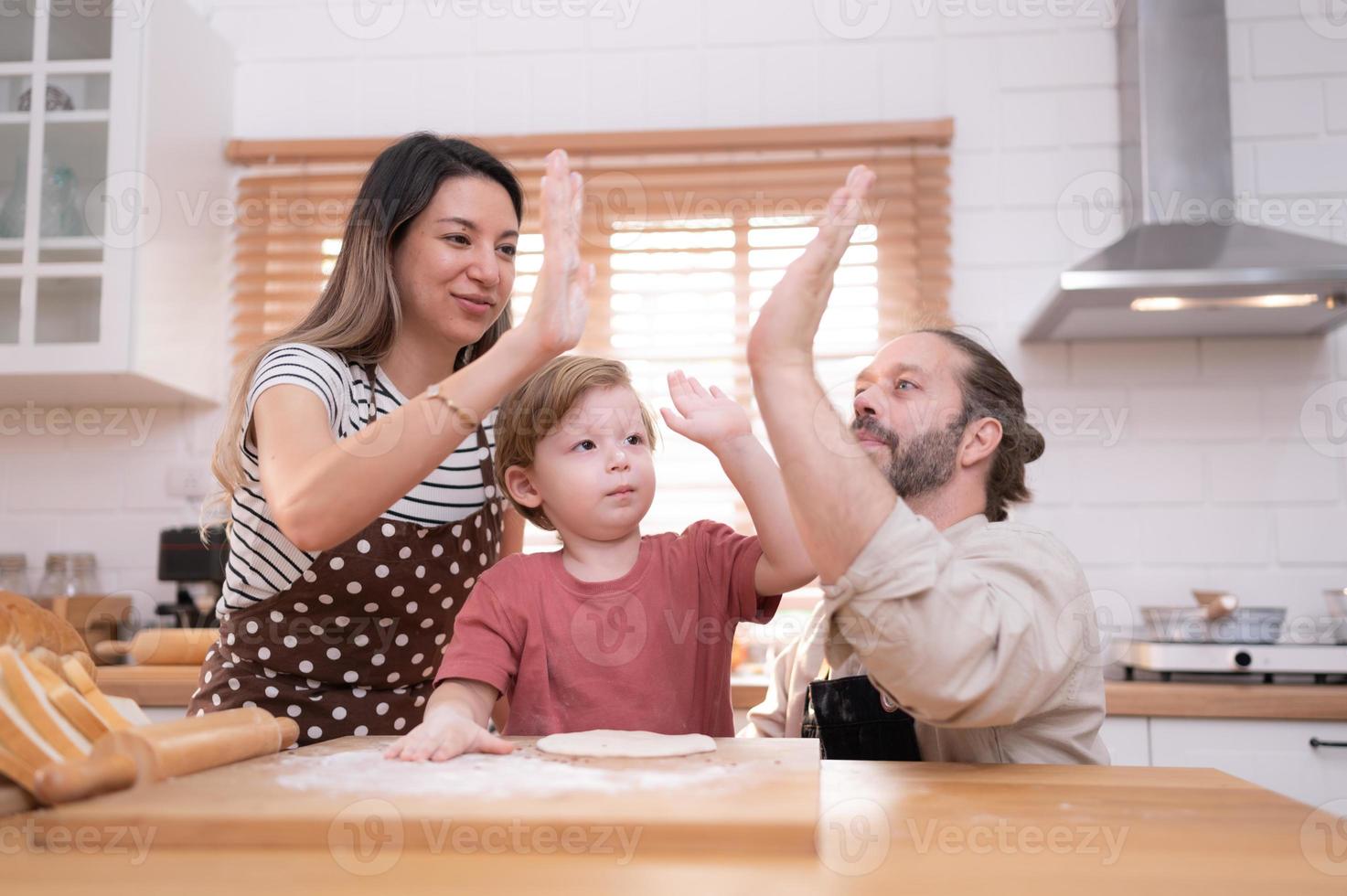 Mom and dad in the kitchen of the house with their small children. Have a good time baking bread and making dinner together. photo