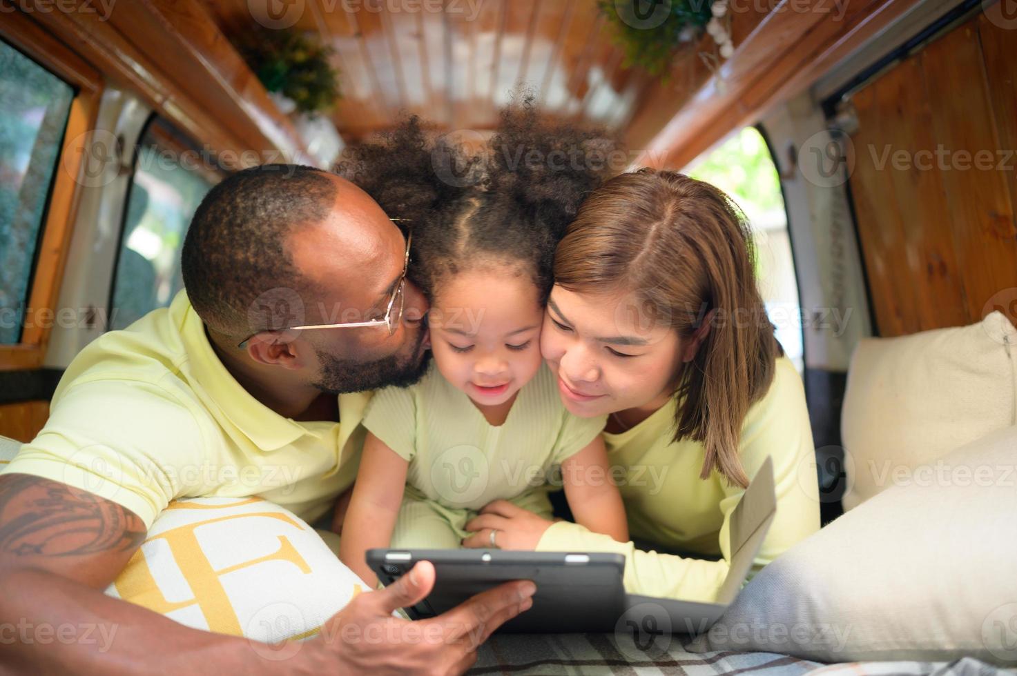 The back of a white classic van, little kids play and learn about the world on their tablet with parents taking care of helping. photo
