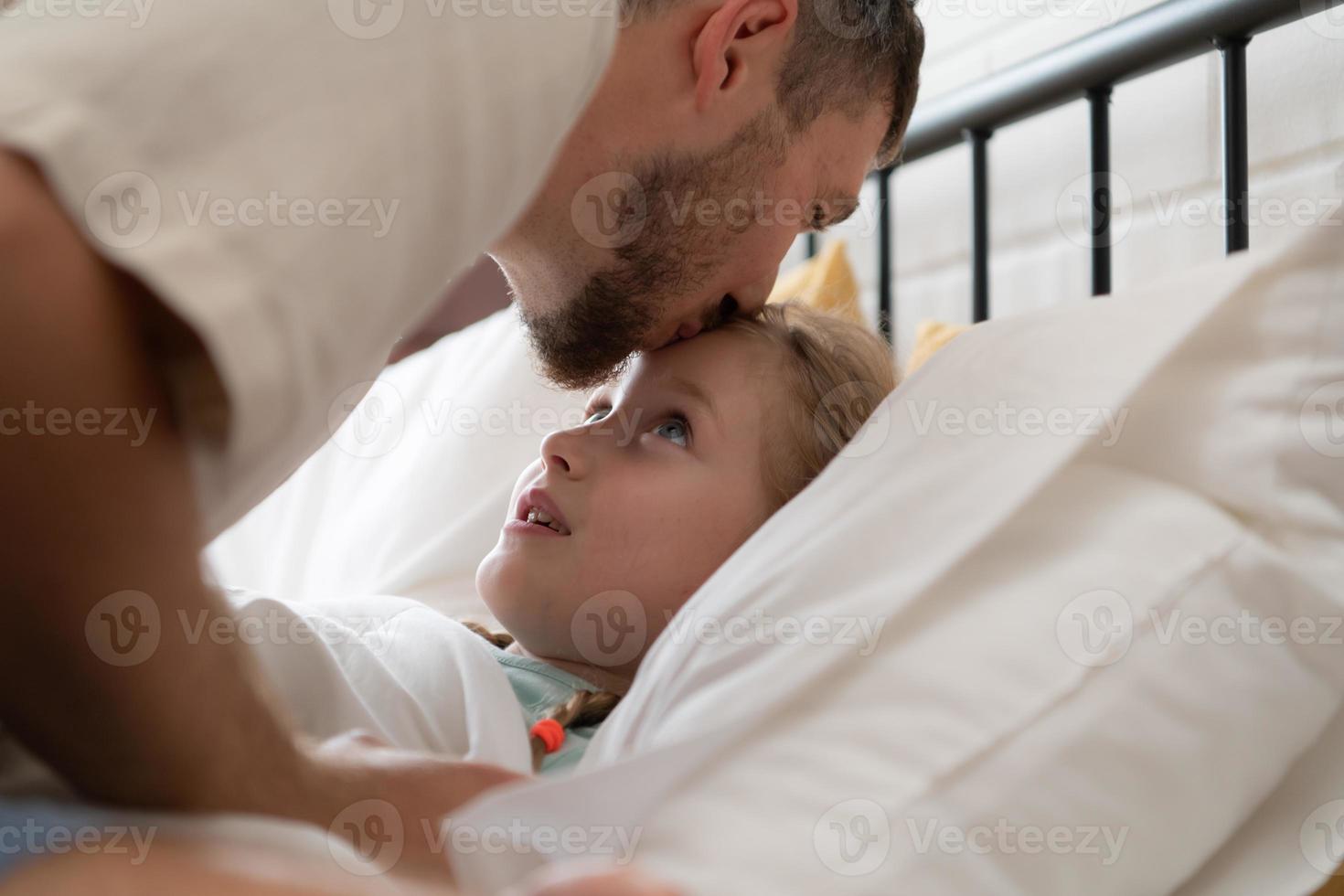 Before retiring to night, a father expresses his affection by kissing his daughter on the forehead. to get a good night's rest photo