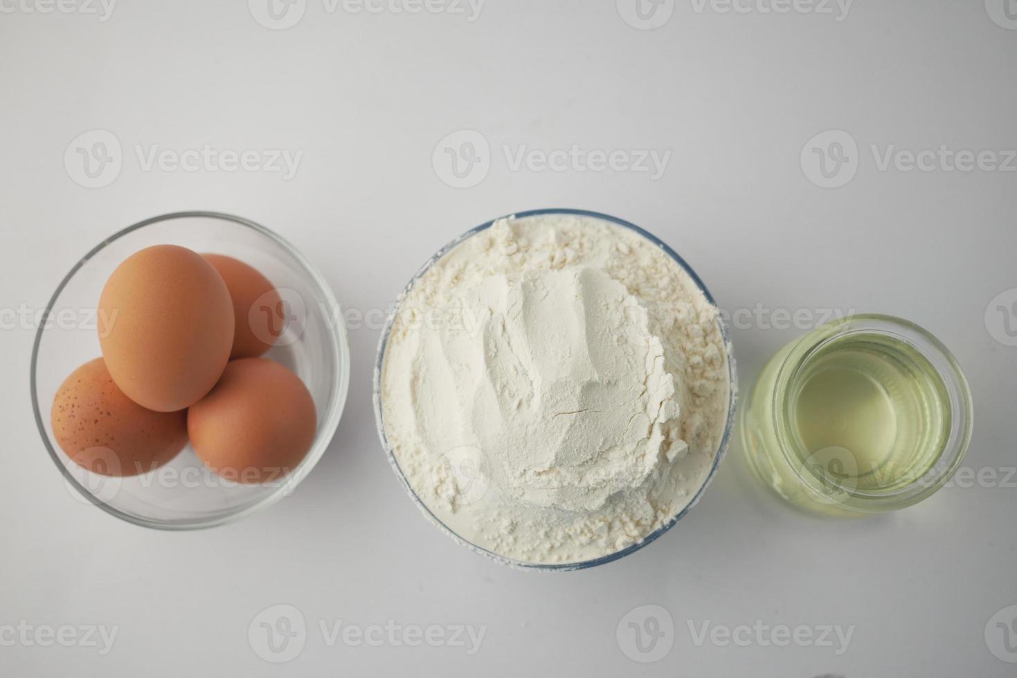 wheat flour in a bowl, eggs and oil on table photo