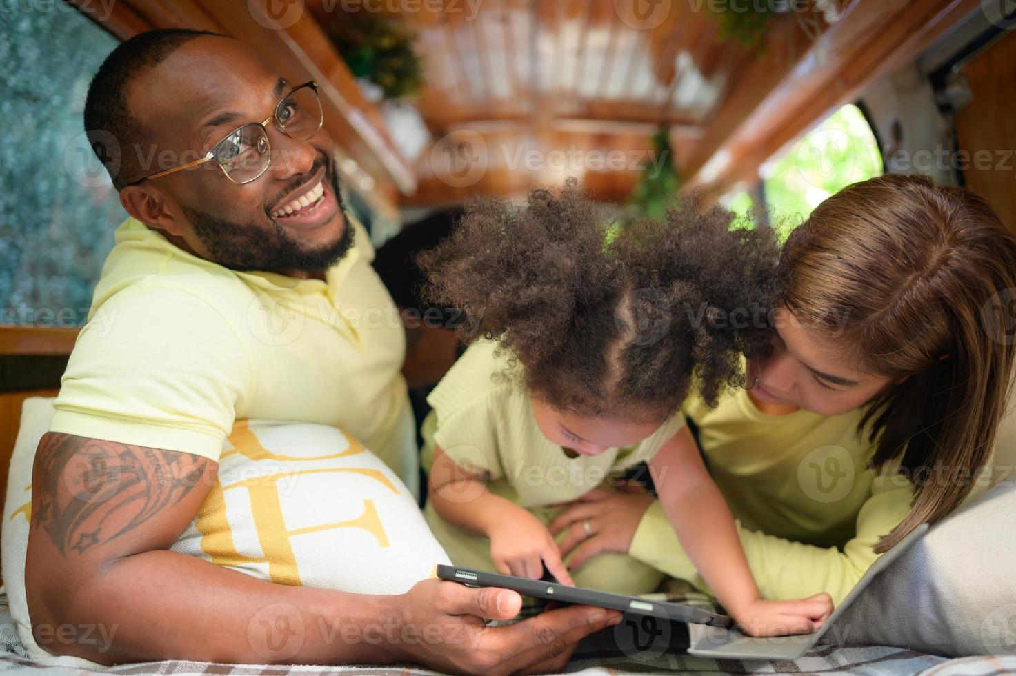 The back of a white classic van, little kids play and learn about the world on their tablet with parents taking care of helping. photo