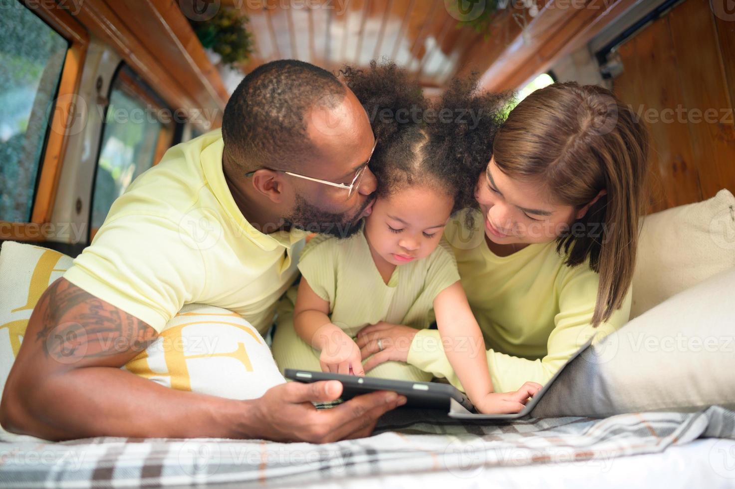 The back of a white classic van, little kids play and learn about the world on their tablet with parents taking care of helping. photo