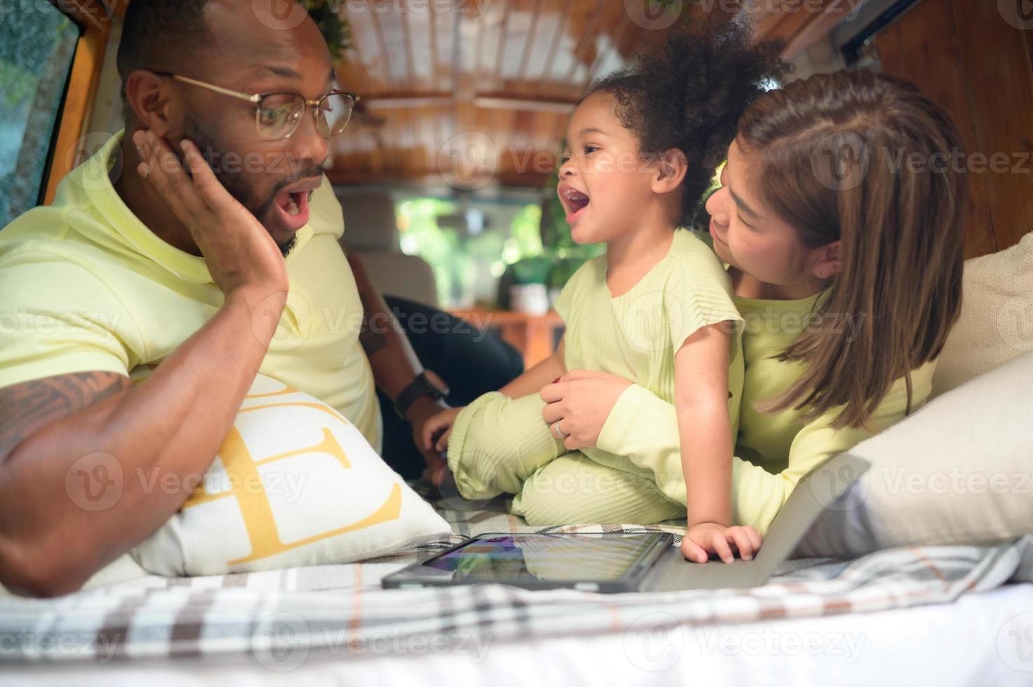 The back of a white classic van, little kids play and learn about the world on their tablet with parents taking care of helping. photo
