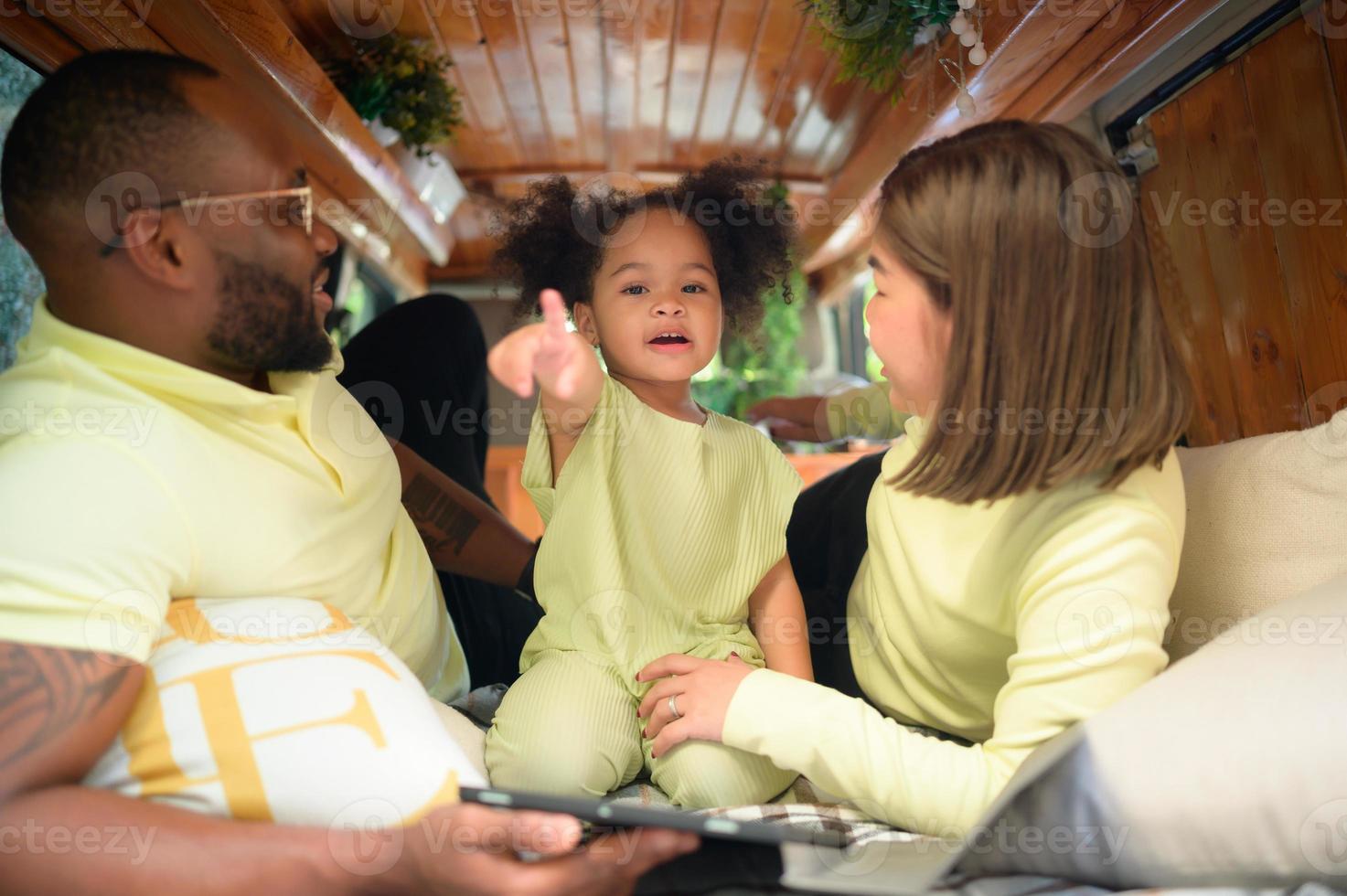 The back of a white classic van, little kids play and learn about the world on their tablet with parents taking care of helping. photo