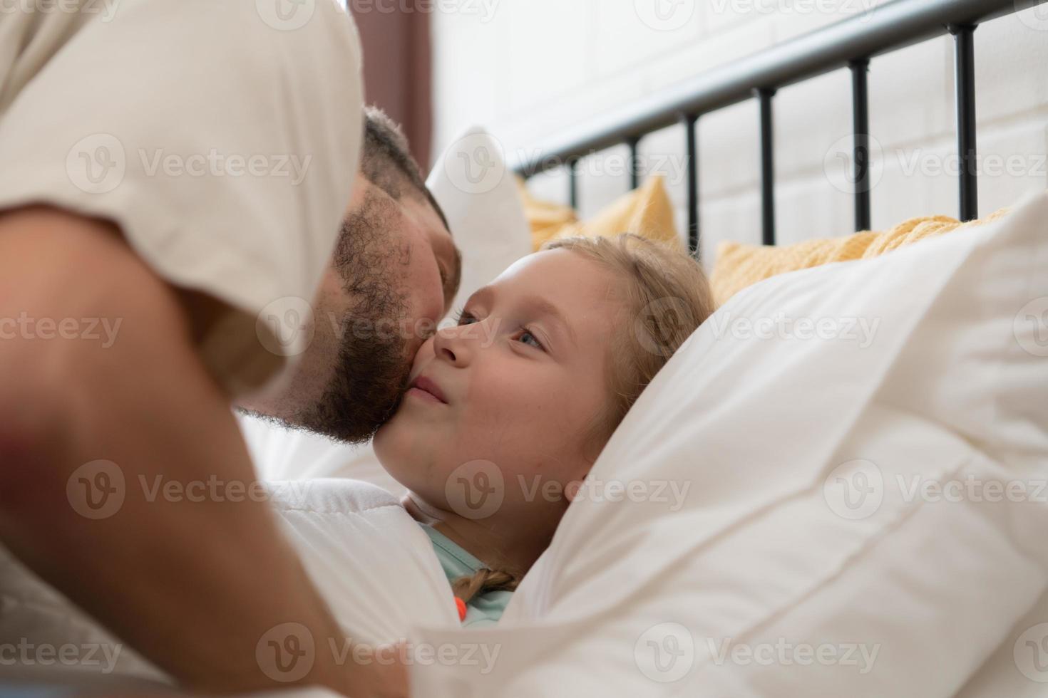 Before retiring to night, a father expresses his affection by kissing his daughter on the forehead. to get a good night's rest photo