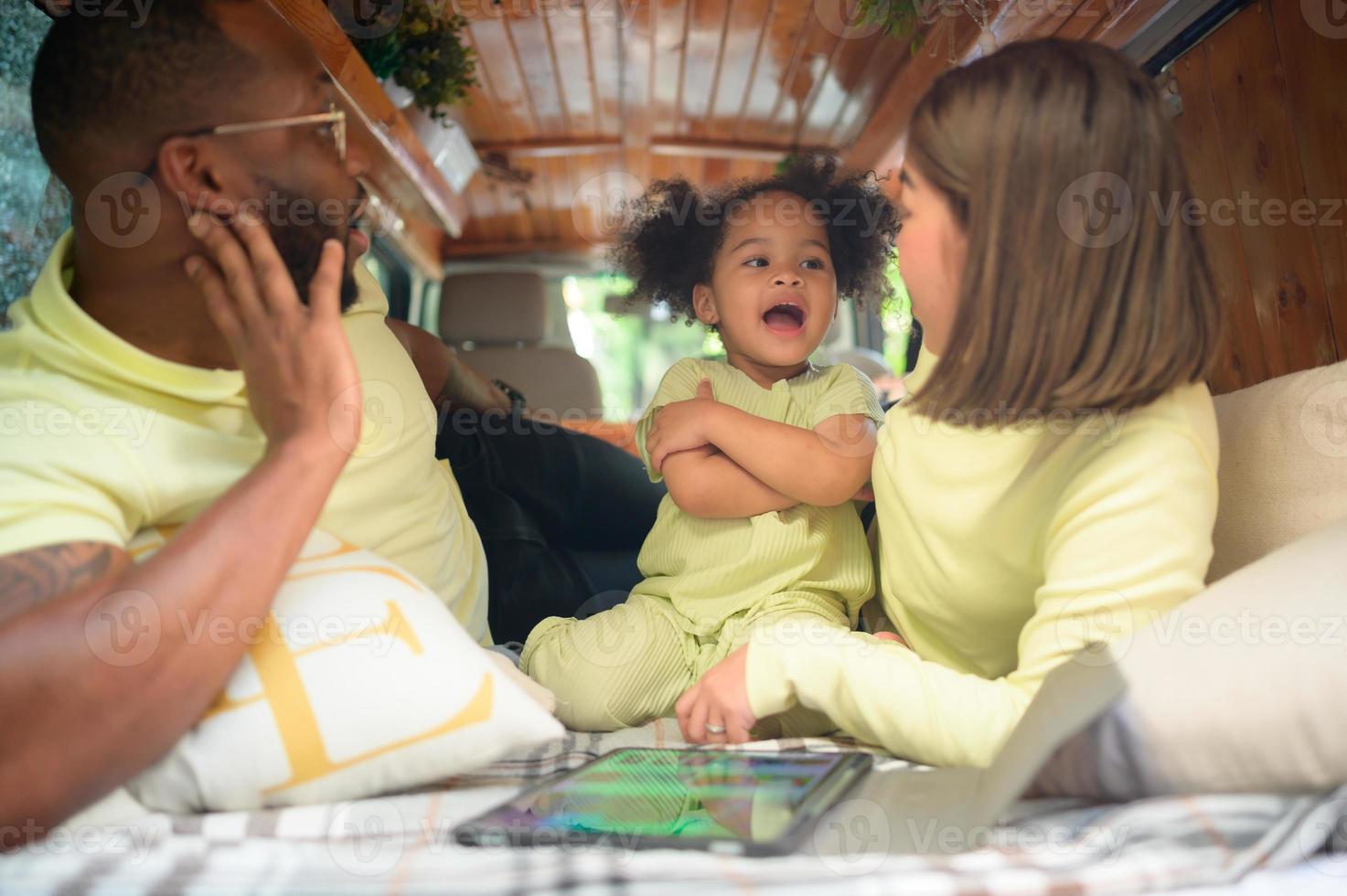 The back of a white classic van, little kids play and learn about the world on their tablet with parents taking care of helping. photo