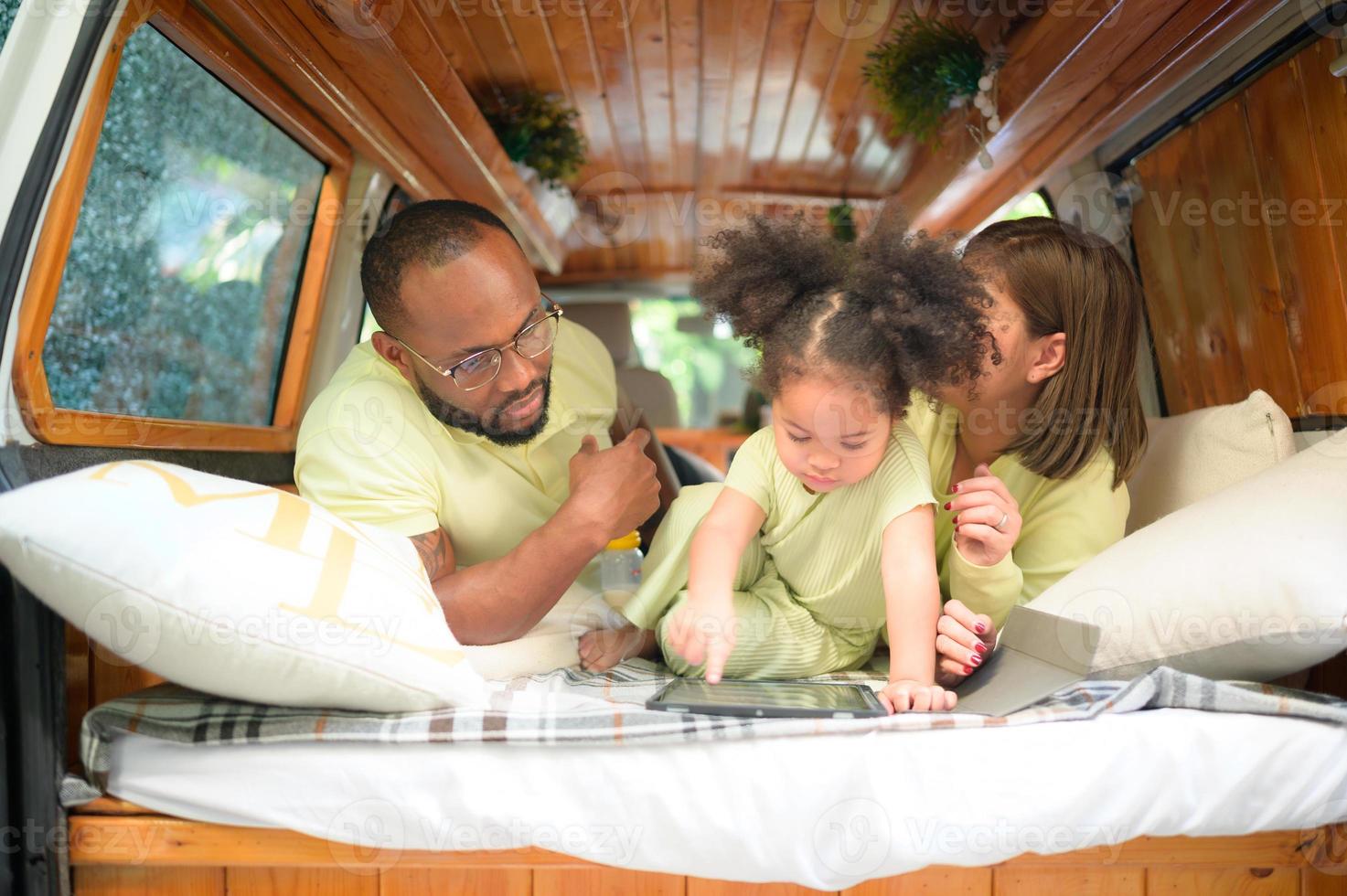 The back of a white classic van, little kids play and learn about the world on their tablet with parents taking care of helping. photo