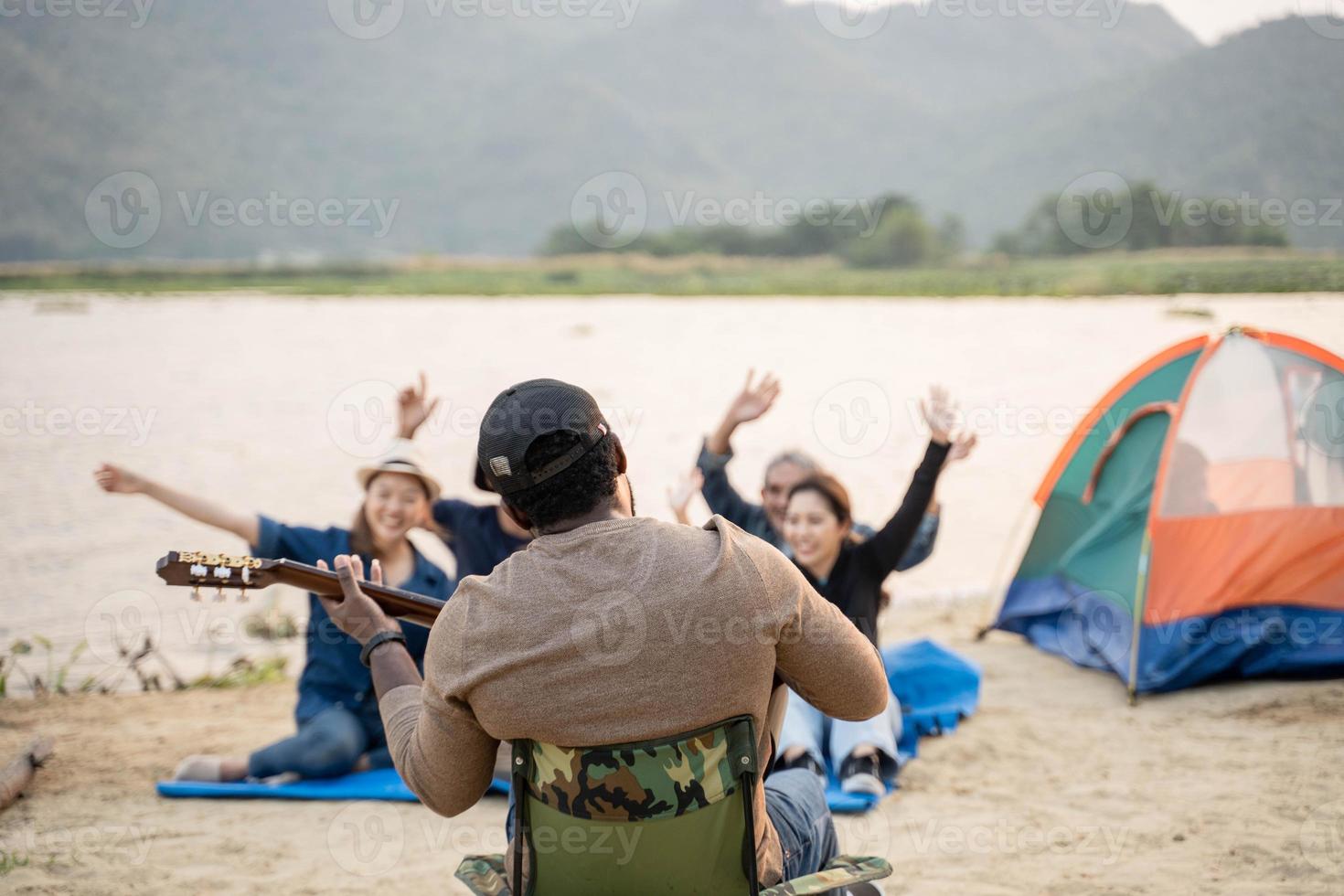 back view at man have fun playing guitar with friend camping at the beach. singing , laughing, playing guitar photo