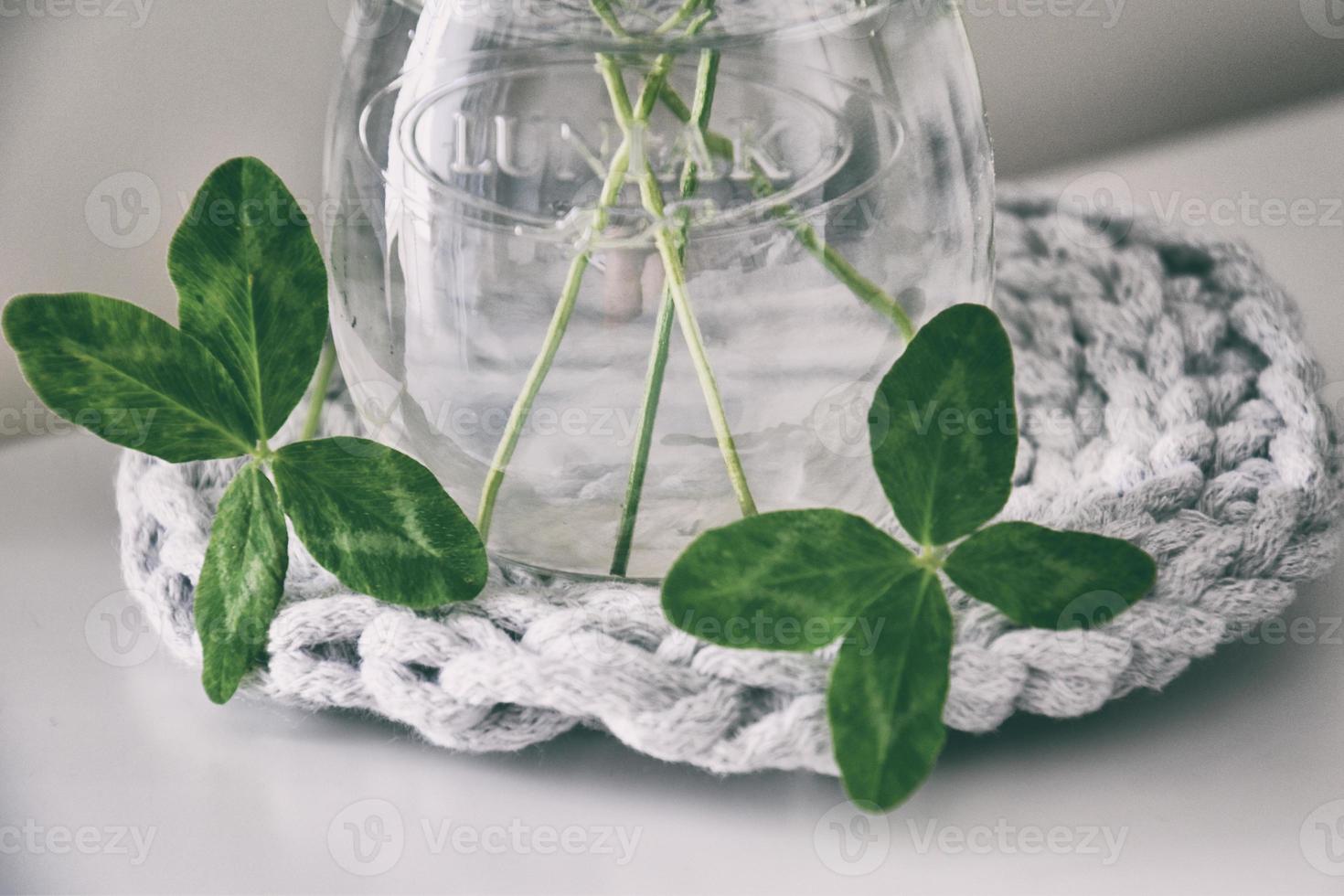 un ramo de flores de l campo cuatro hojas tréboles en un pequeño florero en un ligero suave antecedentes foto