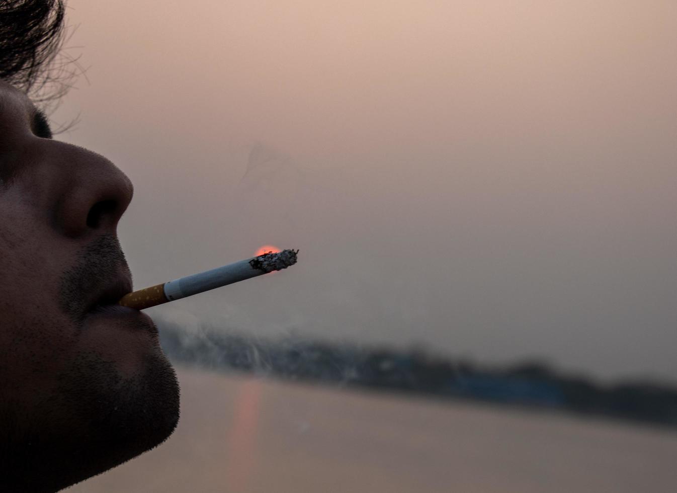 Man smoking a cigarette on a sunset background. Cigarette addiction concept with nature background. Beautiful nature and sunset view with a man smoking a cigarette. Harmful addiction to nicotine. photo
