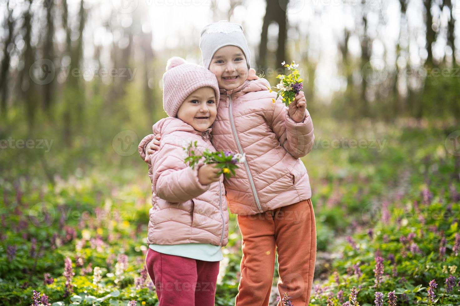 retrato de dos pequeño hermanas con ramo de flores de flores en soleado bosque. al aire libre primavera ocio concepto. foto