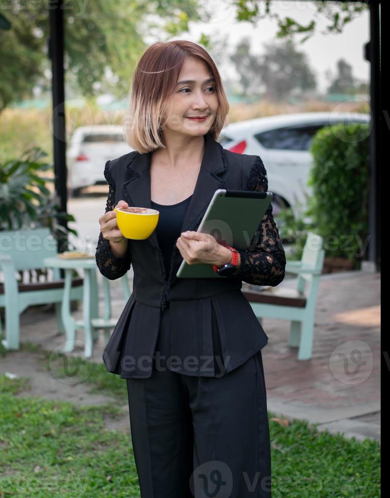 Beautiful business freelance woman standing  the gardens at home hand holding coffee cup,holding tablap and smileing ,Lifestyle relax and chill concept on holiday. photo