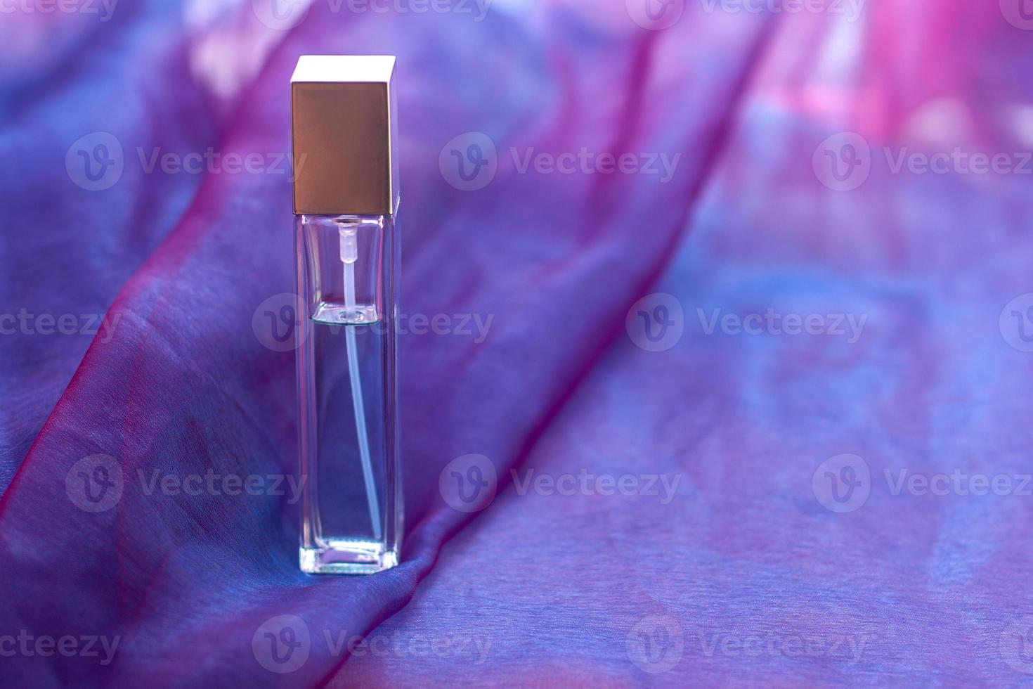 A long faceted bottle with liquid and copy space is placed on a soft cloth. Elongated glass vial. Blank for mock up. Horizontal. photo