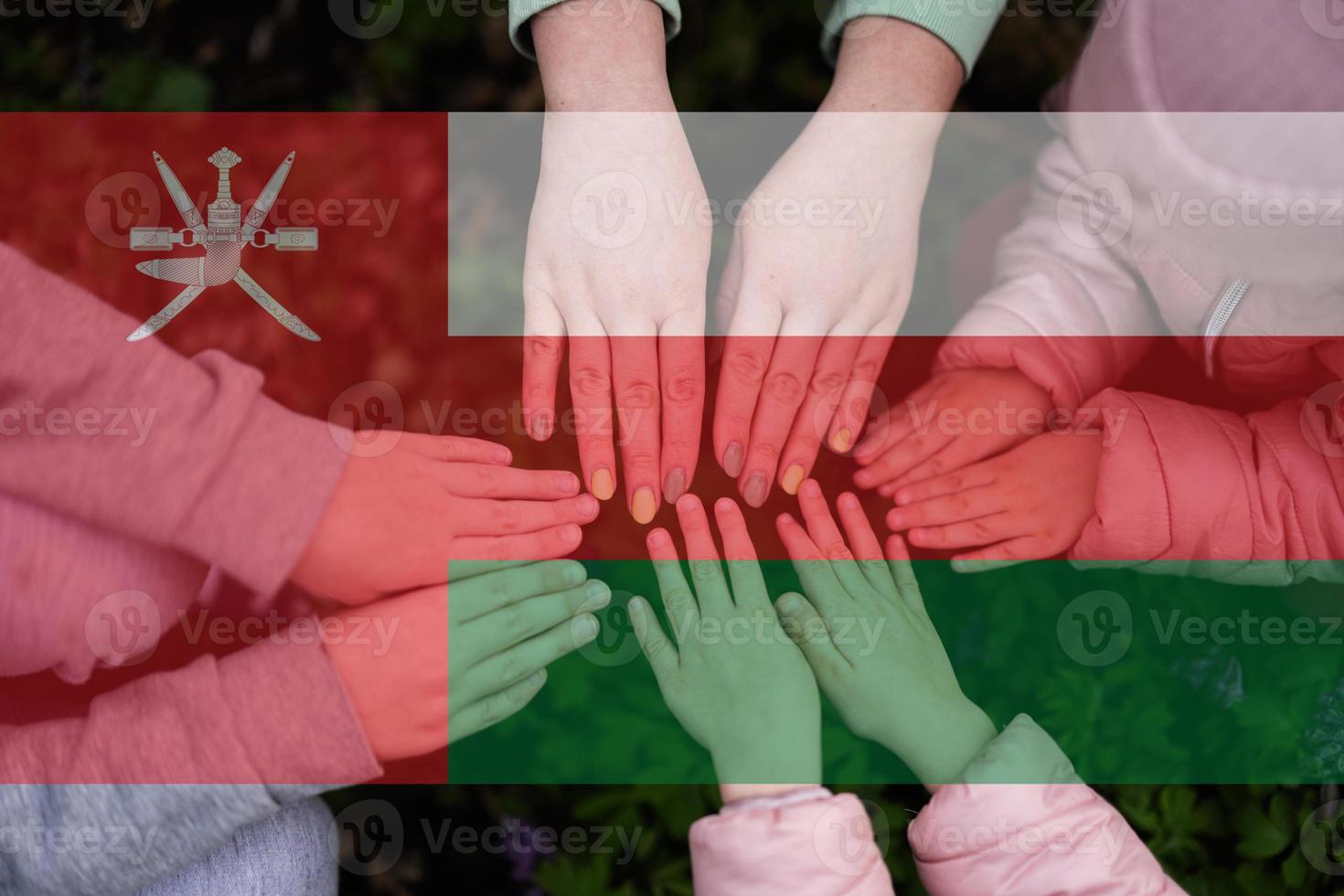 Hands of kids on background of Oman flag. Omani patriotism and unity concept. photo