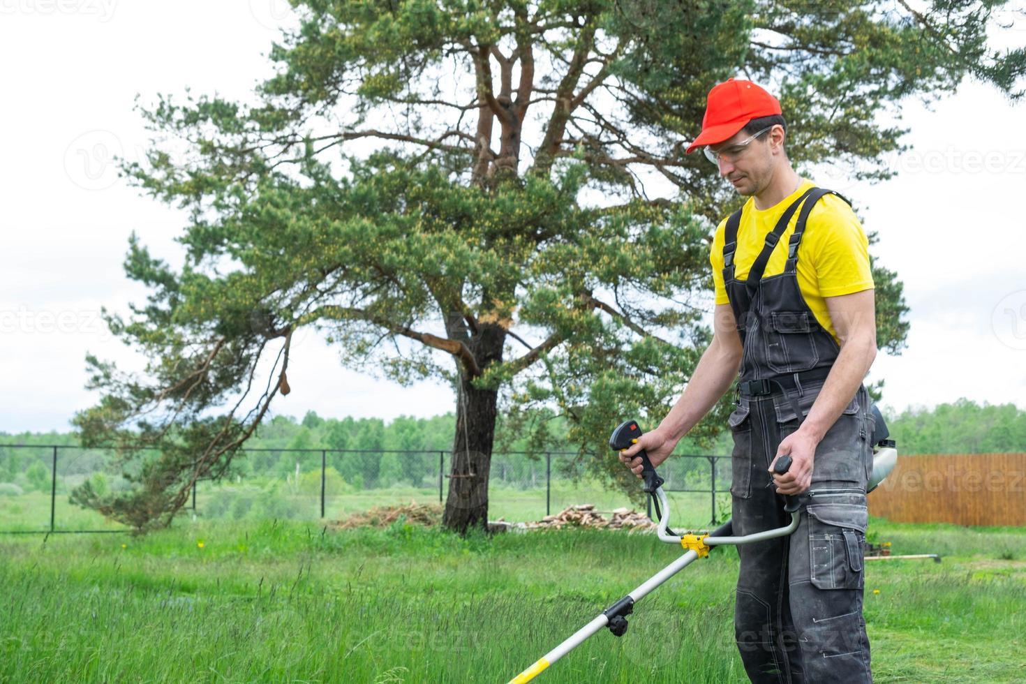 A male gardener mows the green grass of the lawn in the backyard with a gasoline mower. Trimmer for the care of a garden plot photo