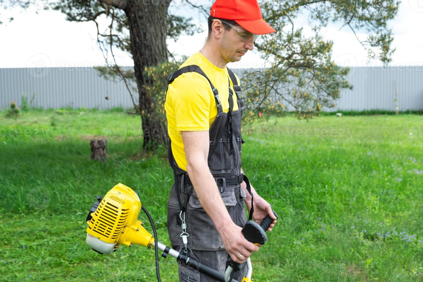 A male gardener mows the green grass of the lawn in the backyard with a gasoline mower. Trimmer for the care of a garden plot photo