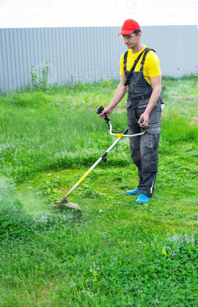 A male gardener mows the green grass of the lawn in the backyard with a gasoline mower. Trimmer for the care of a garden plot photo