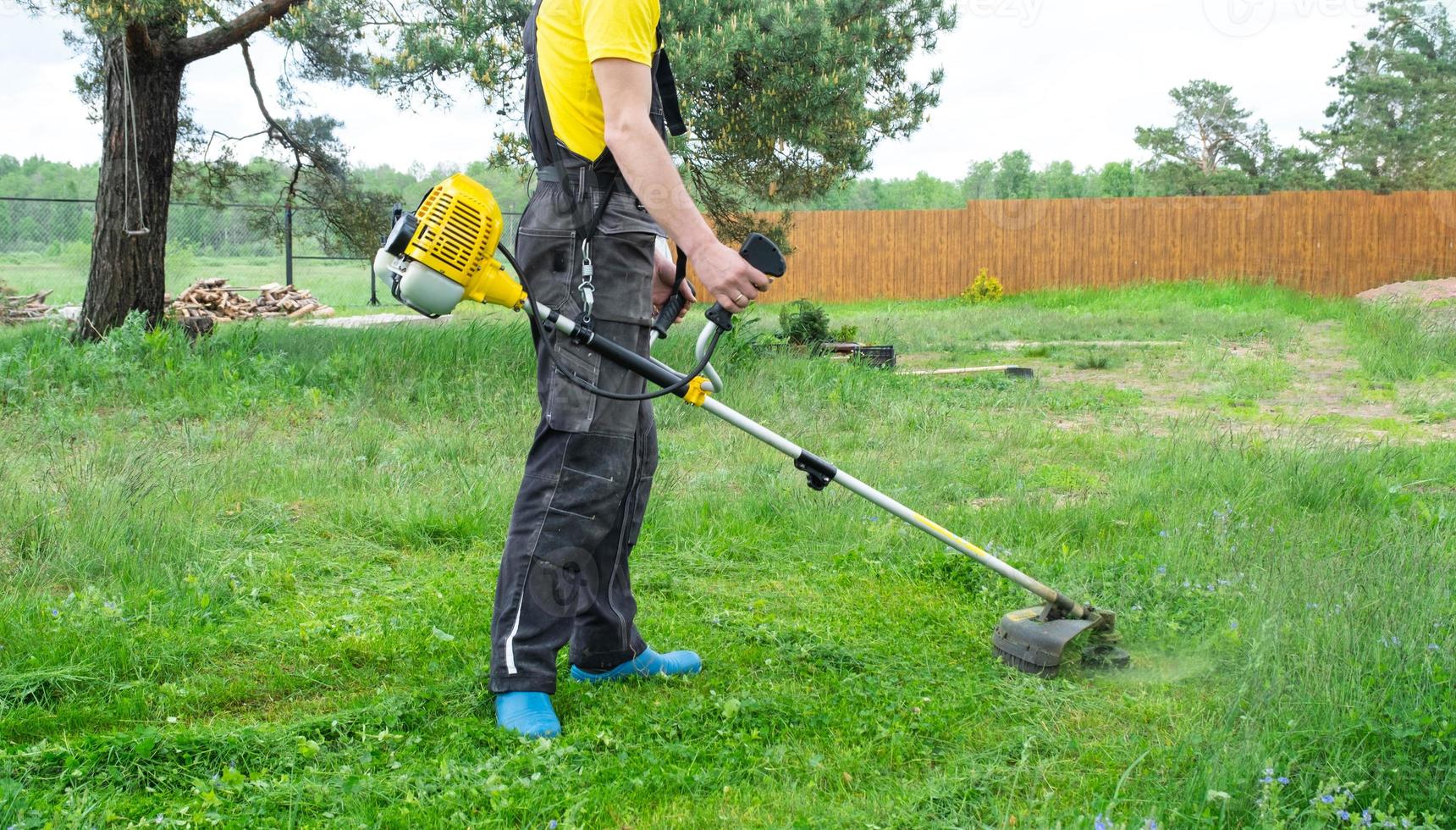 A male gardener mows the green grass of the lawn in the backyard with a gasoline mower. Trimmer for the care of a garden plot photo