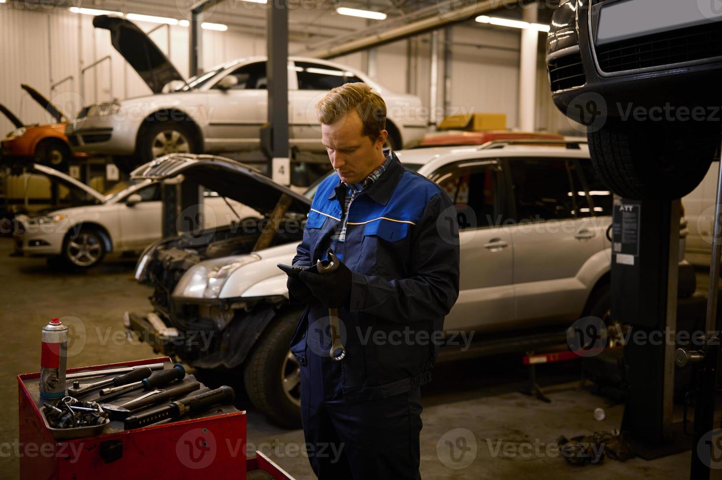 Automobile warranty repair and maintenance concept. Technician, mechanic in professional uniform with wrench at repair shop. photo