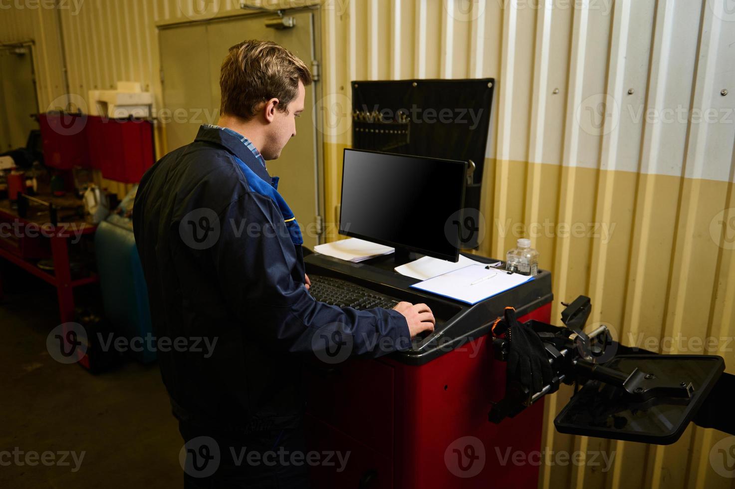 posterior ver de un garaje técnico haciendo cheque lista para reparando auto, mecanografía en teclado y utilizando computadora monitor mientras servicio el automóvil durante garantía mantenimiento en el auto Servicio foto