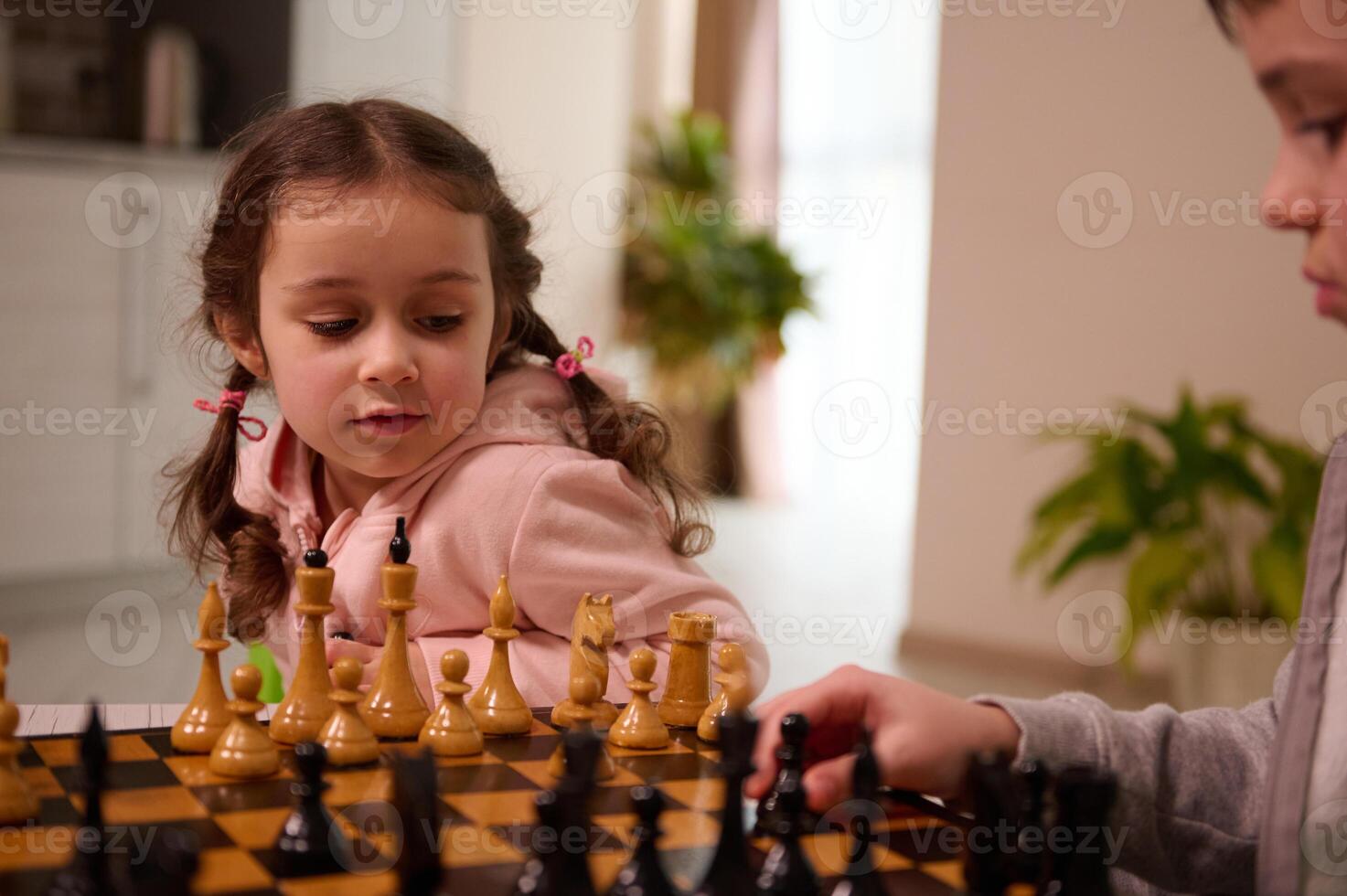 Close-up portrait of a beautiful little European girl playing chess game with her elder brother who picks up a chess piece and make his move. Intellectual smart development board games for kids photo