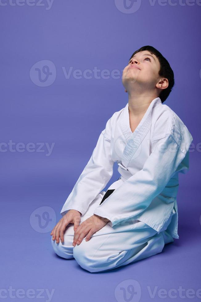 Charming pleasant Caucasian boy in white kimono practicing oriental martial arts, isolated on violet background with copy ad space for text photo