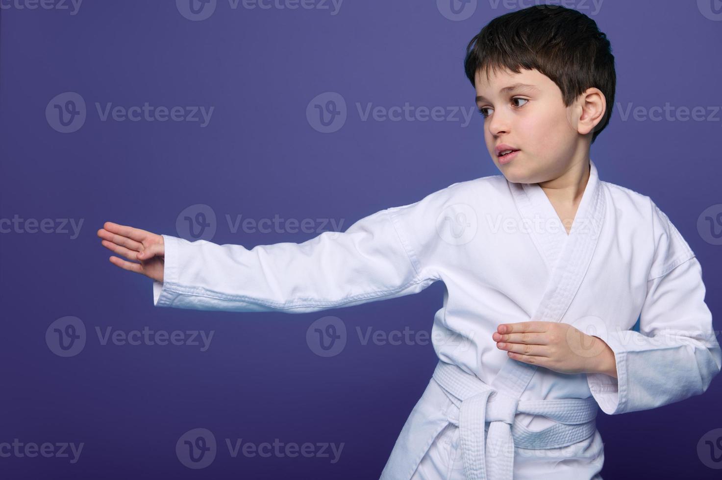 Aikido wrestler European 10 years old boy in white kimono improves his fighting skills, isolated on purple background copy space. Oriental martial arts. photo