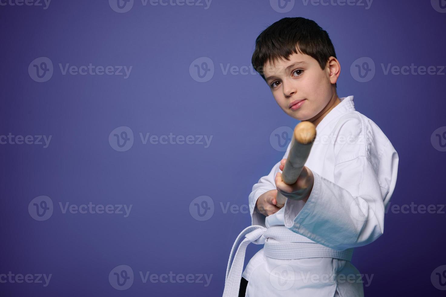 Oriental martial arts practice. Aikido wrestler in white kimono with wooden weapon bokken practices fighting skills on purple background copy ad space photo