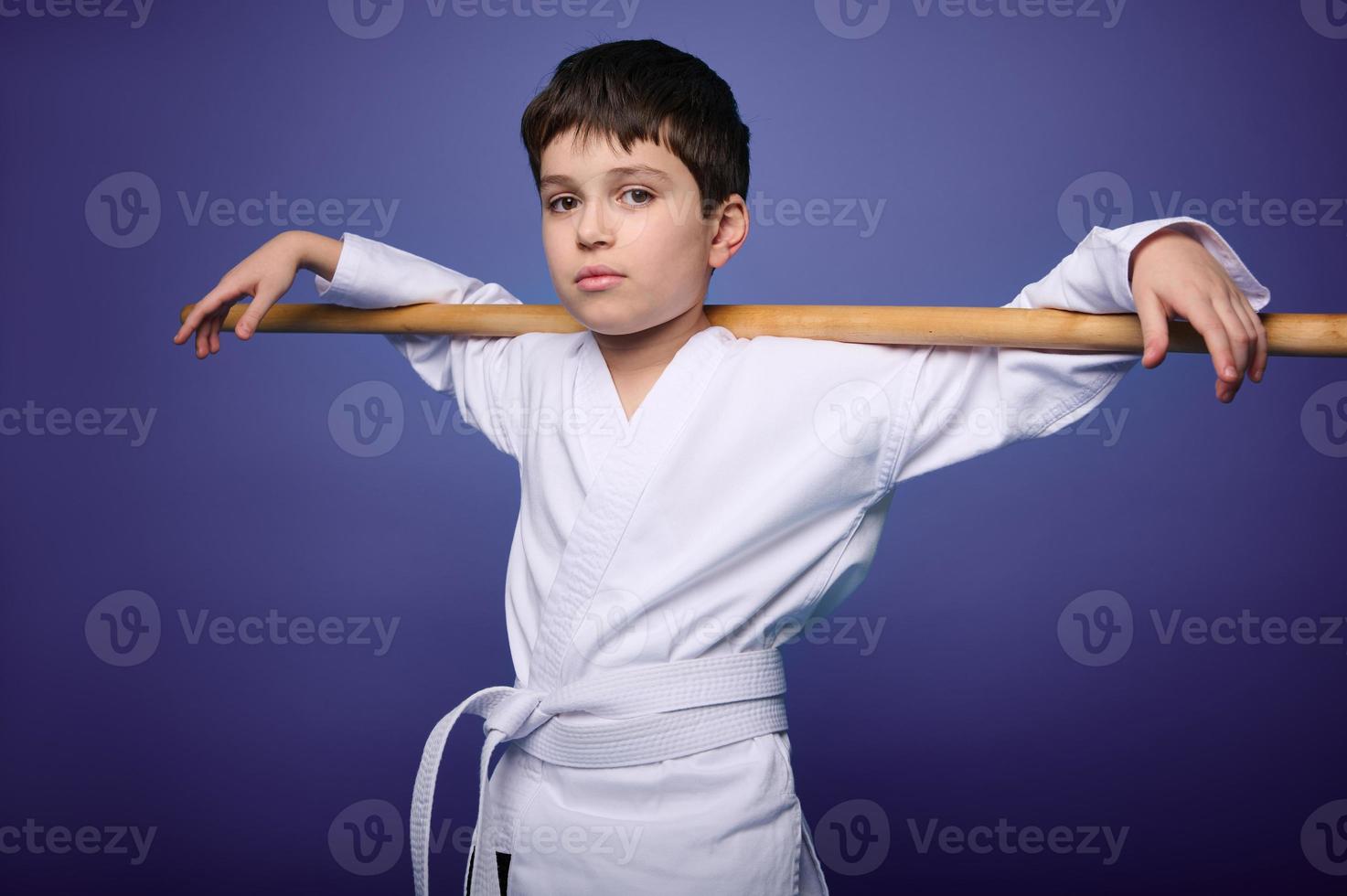 Confident strong Caucasian Oriental martial arts wrestler posing with wooden aikido weapon against violet background with copy ad space photo