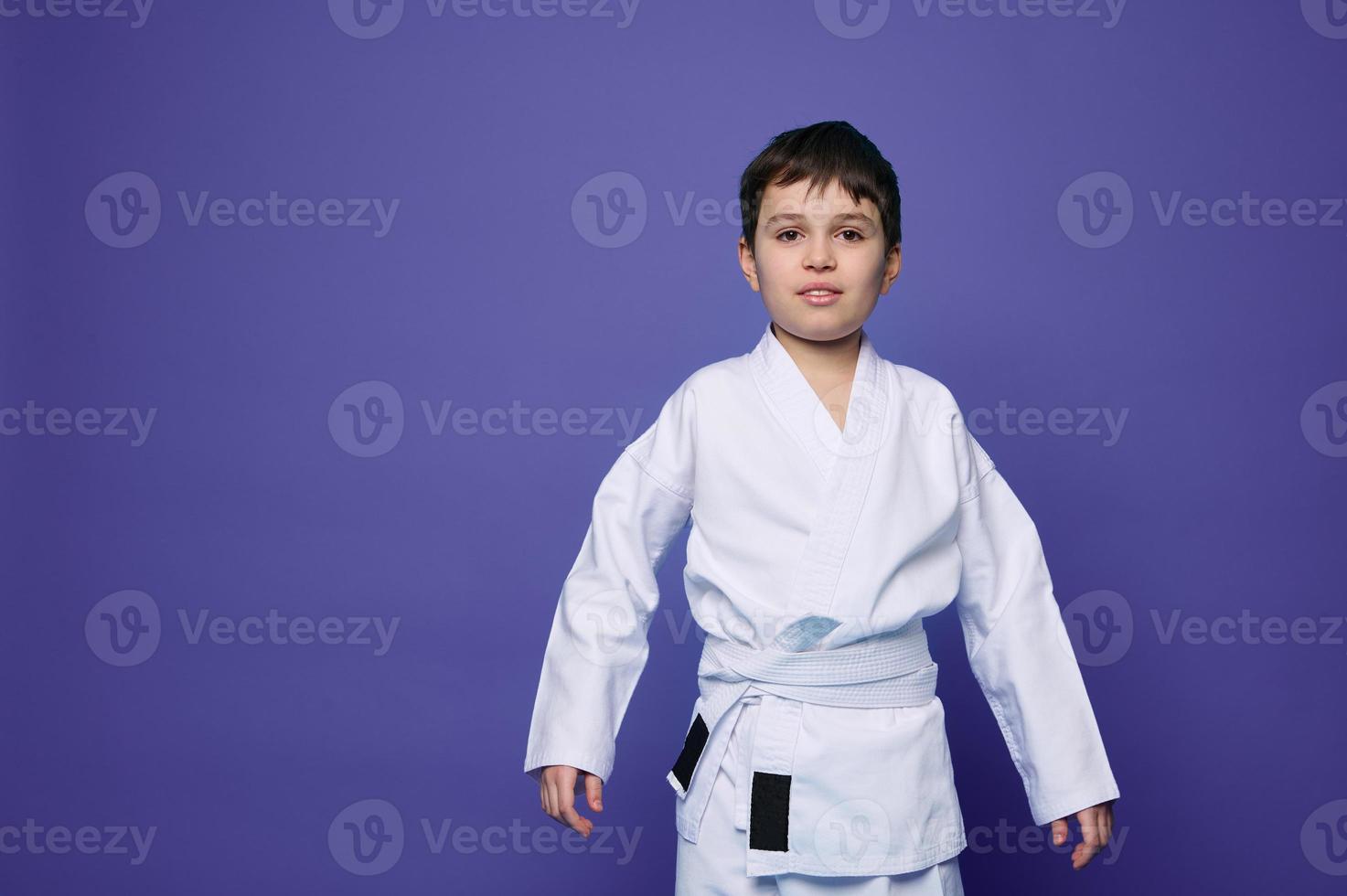 Charming confident aikido wrestler- Caucasian teenager in white kimono isolated on purple background with copy ad space. Oriental martial arts concept photo