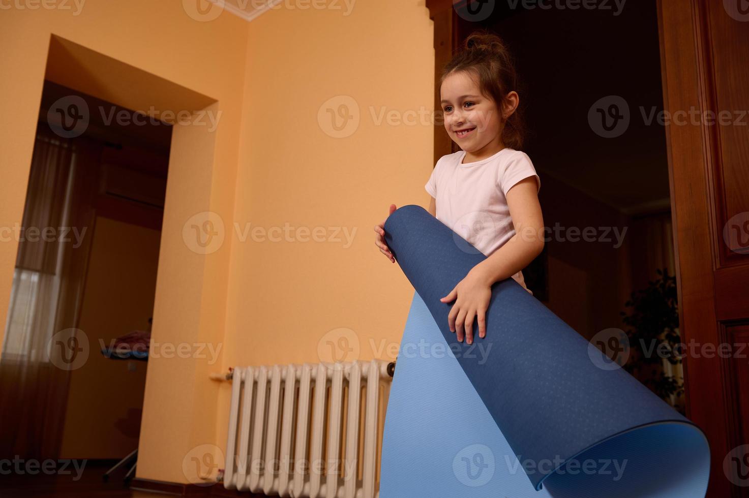 Sporty little girl holding yoga mat while practicing meditation or doing stretching exercises at cozy homely atmosphere photo