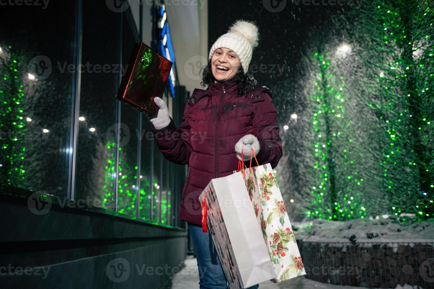 Charming young woman walking down the street with shopping bags with Christmas gift box in her hands. Merry Christmas. photo