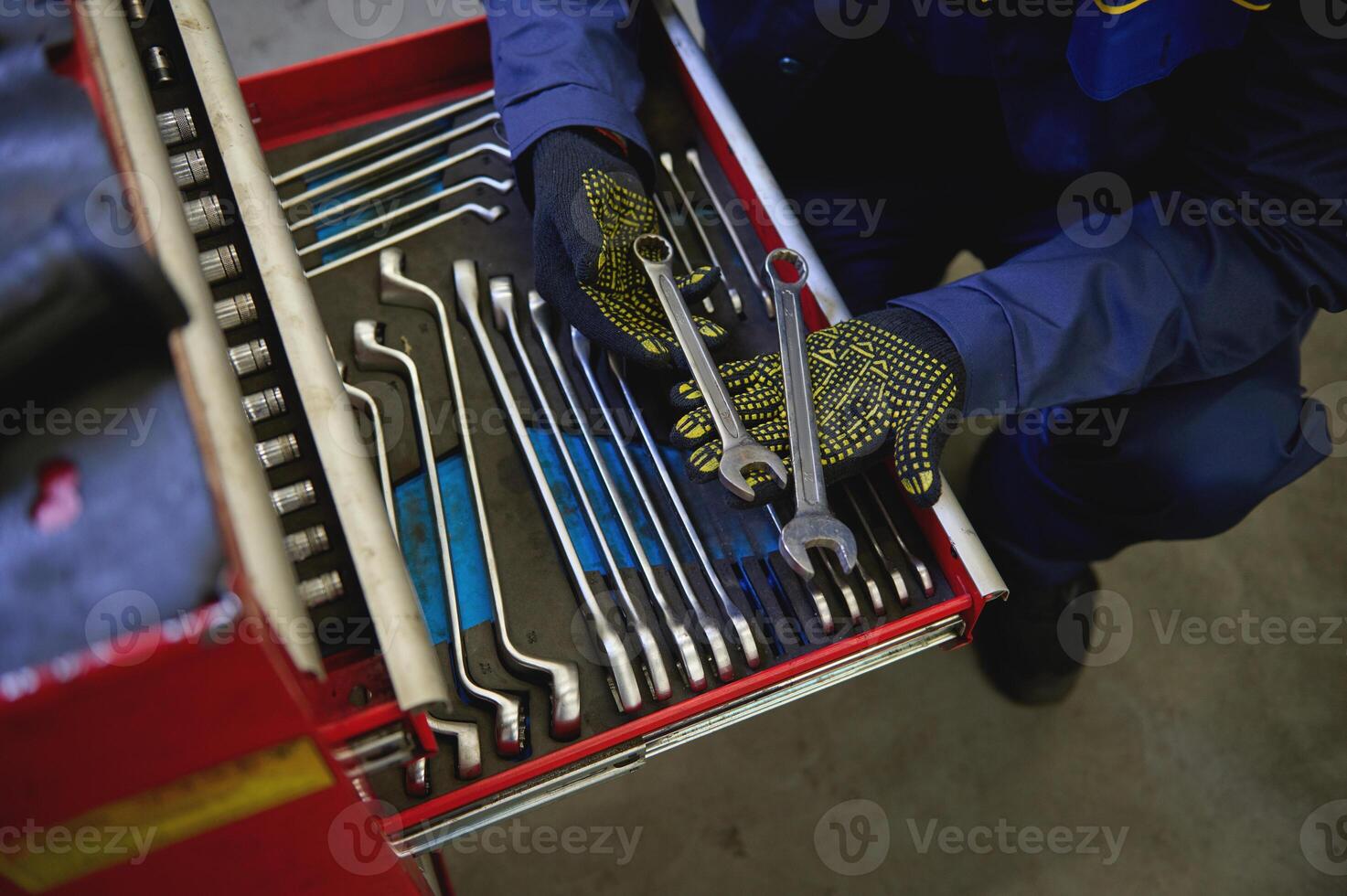 Overhead view of a mechanic holding wrenches above a set of tools from wrenches and heads for unscrewing nuts and bolts in a special cabinet for repair in a car service. Industry and manufacturing. photo