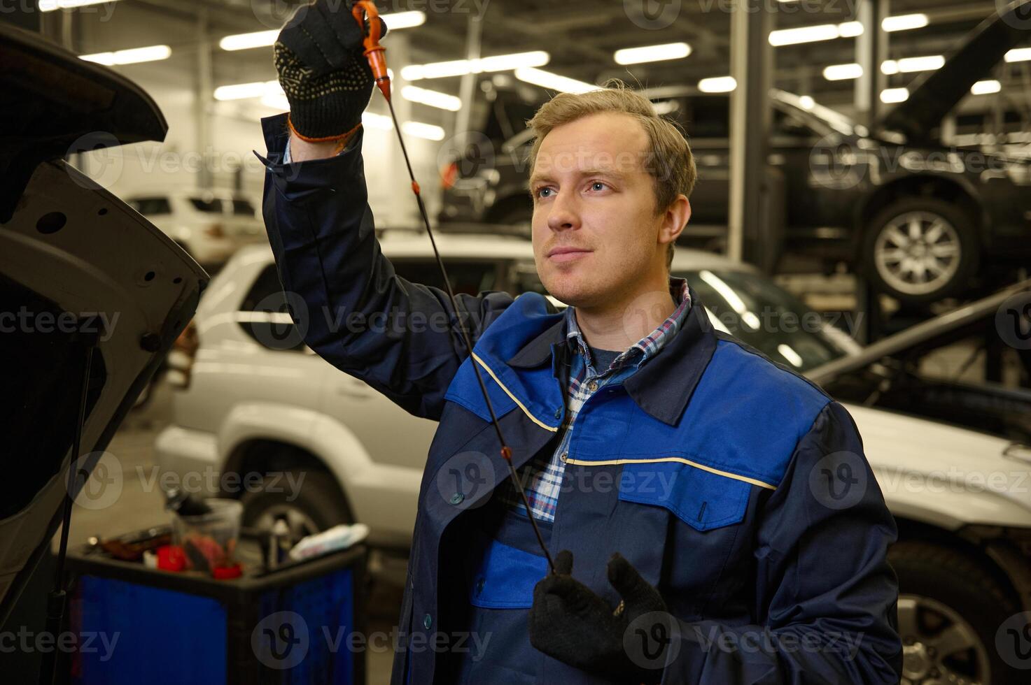 Mechanic in garage examining the car engine oil dipstick checking motor oil level at a car. Car engineer technician in the car repair shop. Automobile maintenance and auto service concept photo