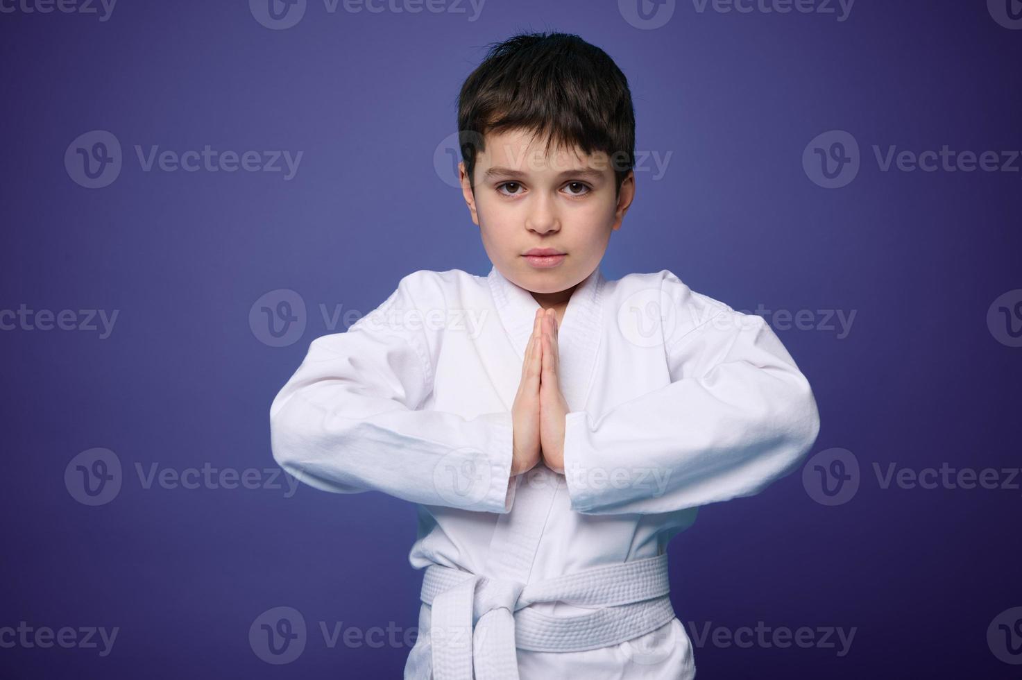 Waist length portrait of a strong European teenage boy, aikido fighter practicing martial skills against violet wall background, copy ad space photo