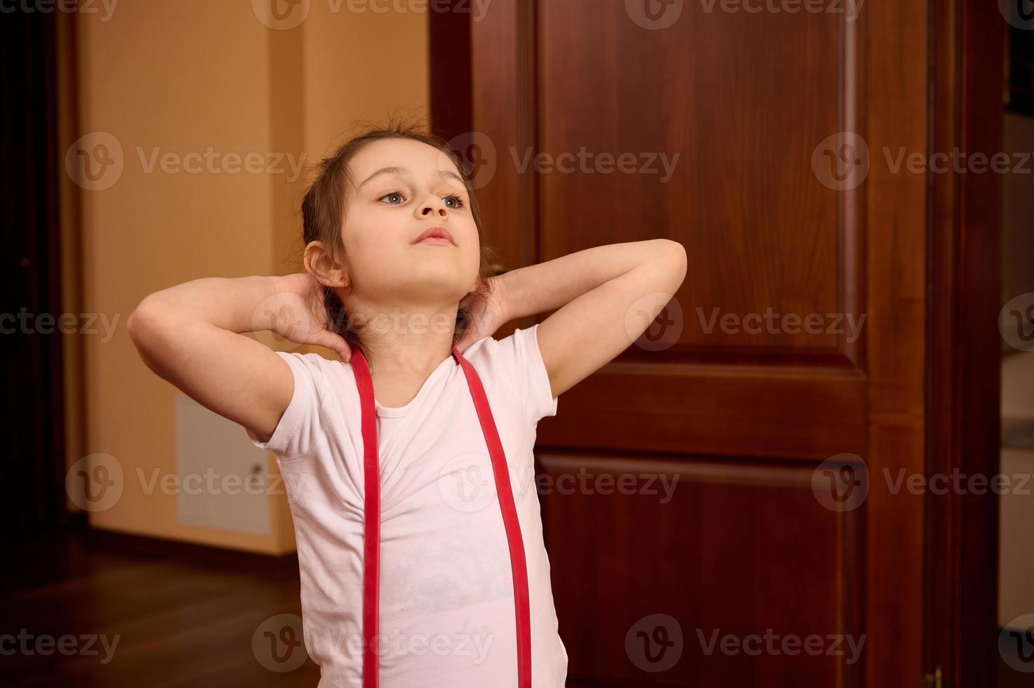 Determined confident Caucasian sporty child girl in sportswear, exercising with elastic fitness band on gym mat. photo