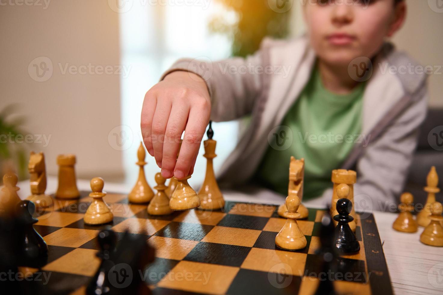 Focus on the hand of a blurred handsome boy holding a chess piece above the chessboard and making a move during the game. Smart intellectual board games for kids, logic development, education concept photo