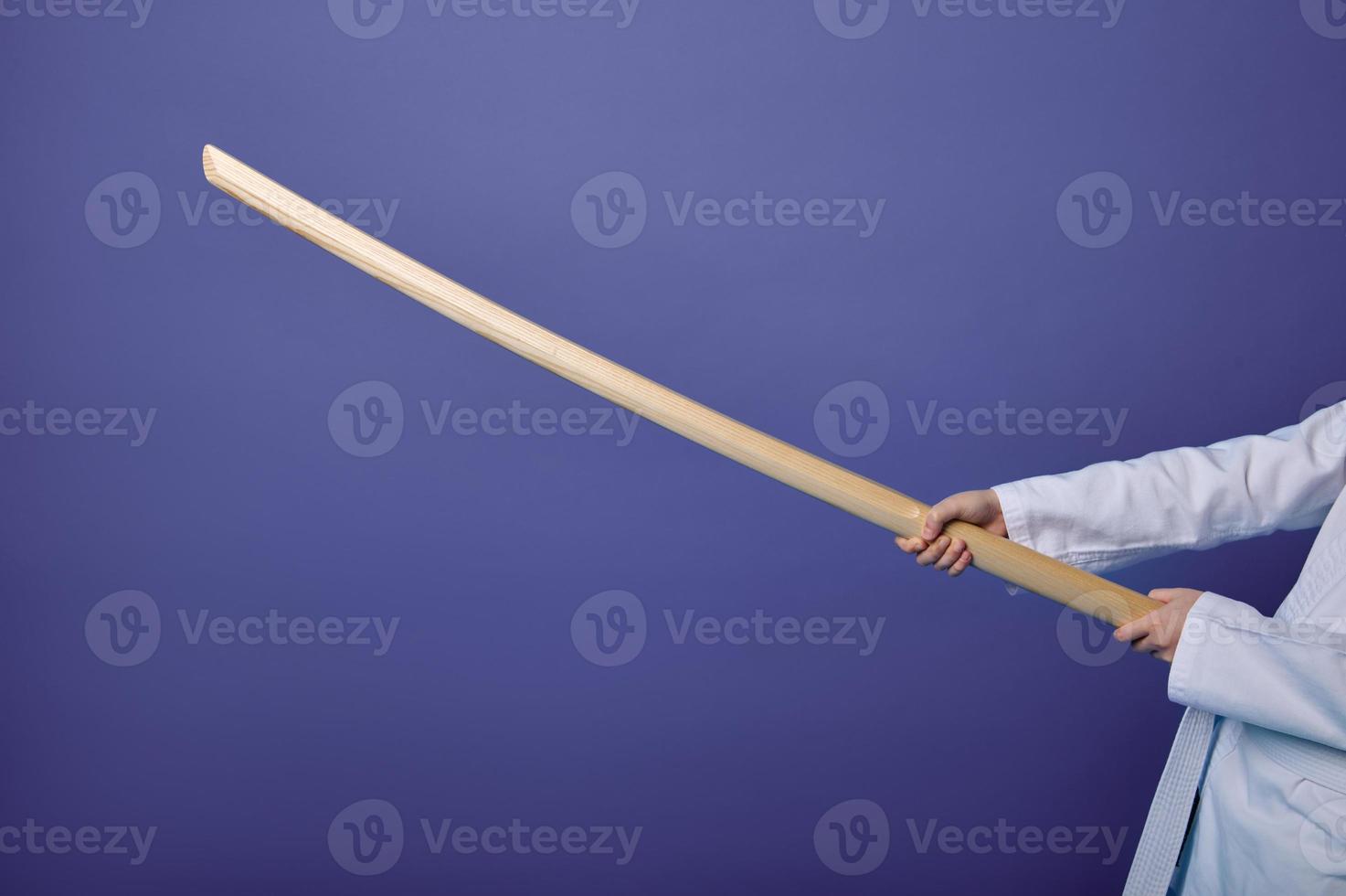 Close-up of aikido fighter's hands holding wooden weapon - sword katana- practicing Oriental martial arts skills on purple background with copy space photo