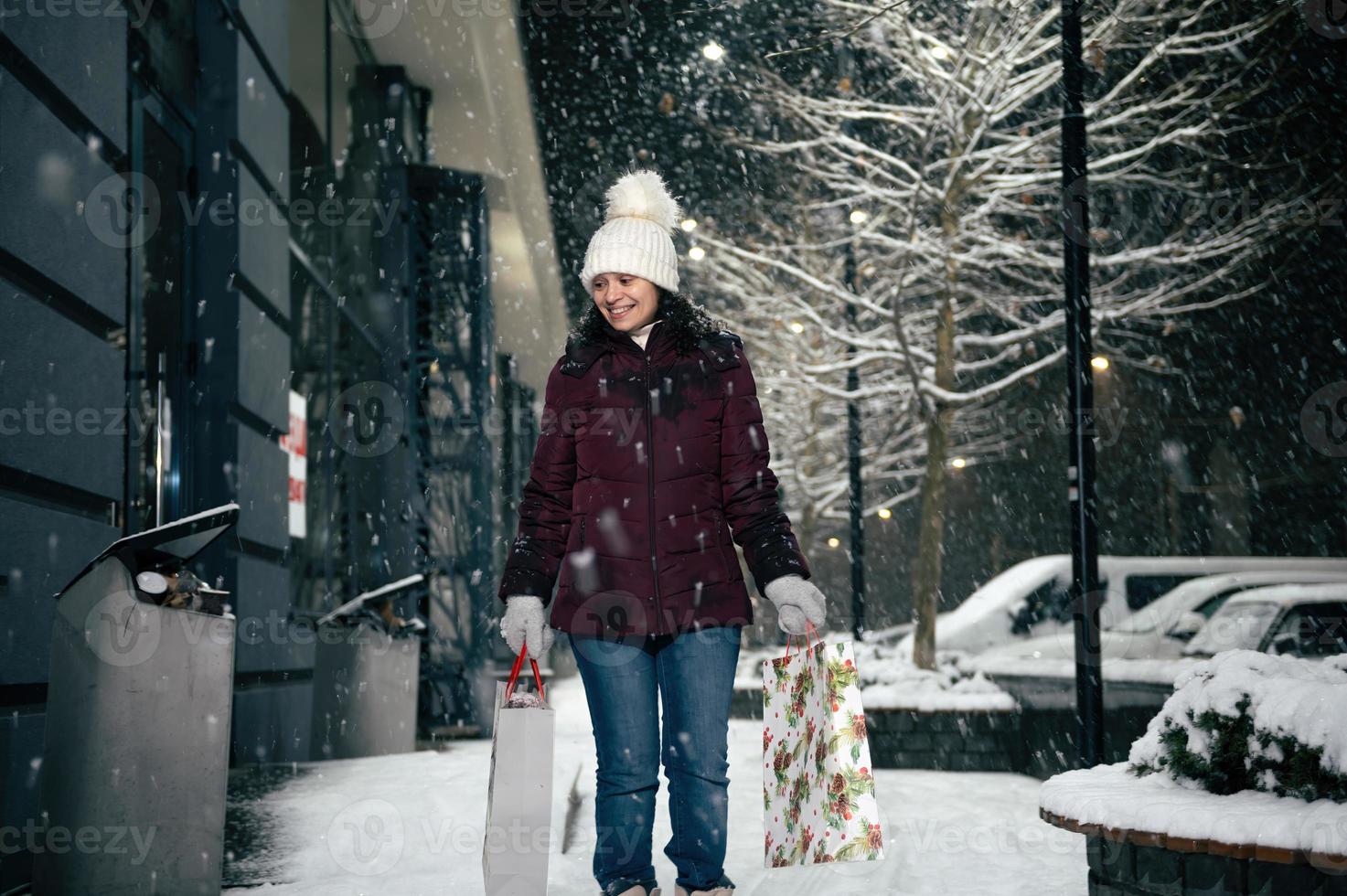 encantador joven mujer caminando abajo el calle con compras pantalones con Navidad regalo caja en su manos. alegre Navidad. foto