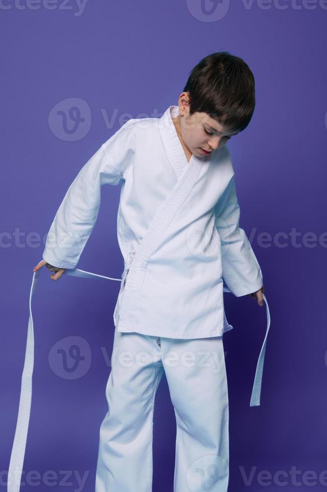 Handsome child, Caucasian teenage boy, aikido wrestler putting on white kimono isolated on purple background with copy space for advertising text photo