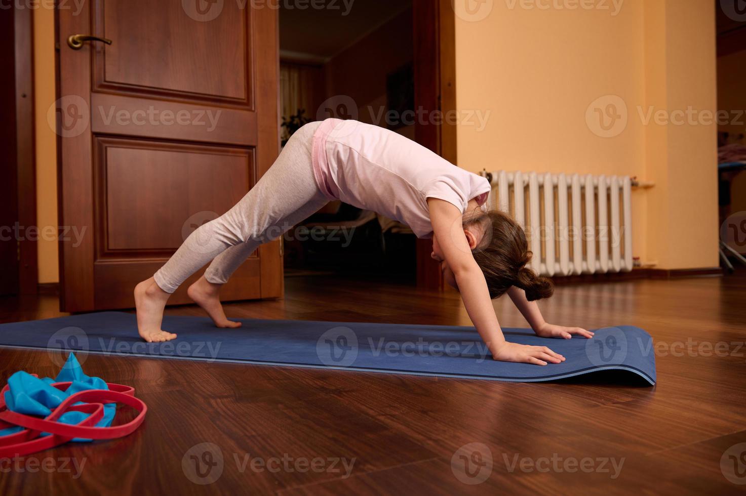 Little girl in sportswear, stretching in adho mukha svanasana exercise, downward facing dog pose, working out indoors photo