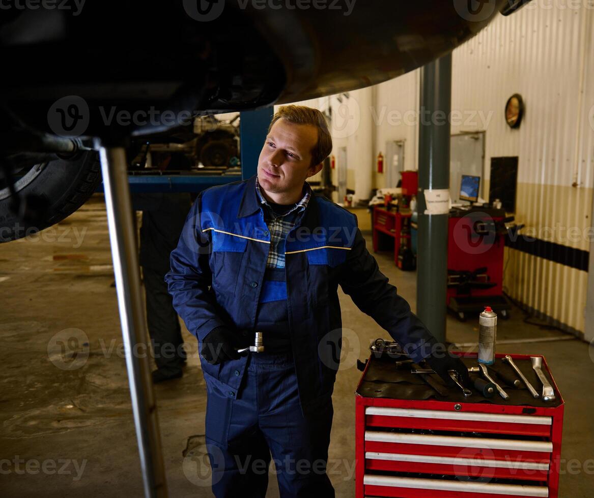 Car engineer, technician, auto mechanic repairing a lifted modern automobile on a hoist in the repair shop garage. Automobile maintenance and auto service concept photo