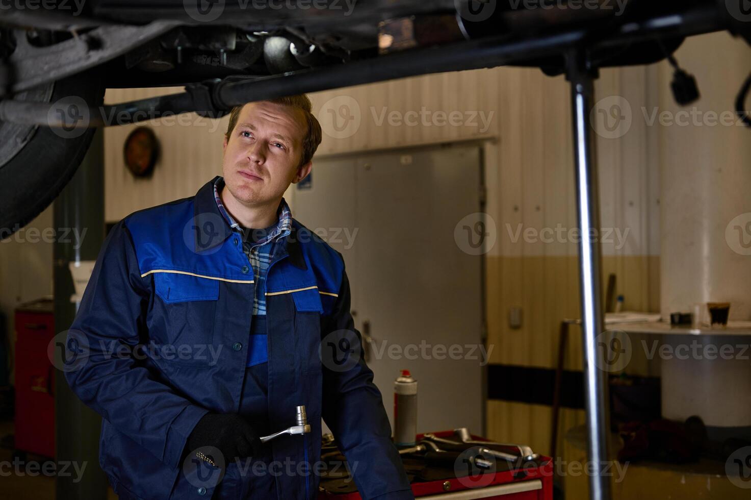 auto mecánico en uniforme inspeccionando un levantado coche en un izar, mientras haciendo Lista de Verificación para garantía reparando automóvil en el taller garaje foto