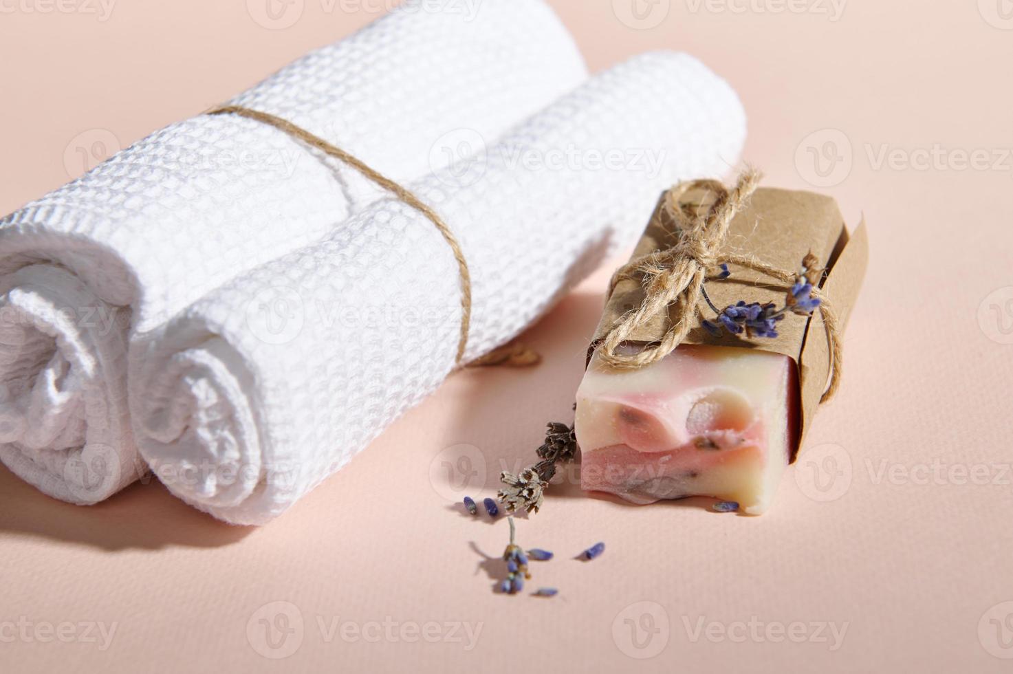 Still life with rolled towels near natural organic soap bar and scattered lavender flowers on isolated pink background photo