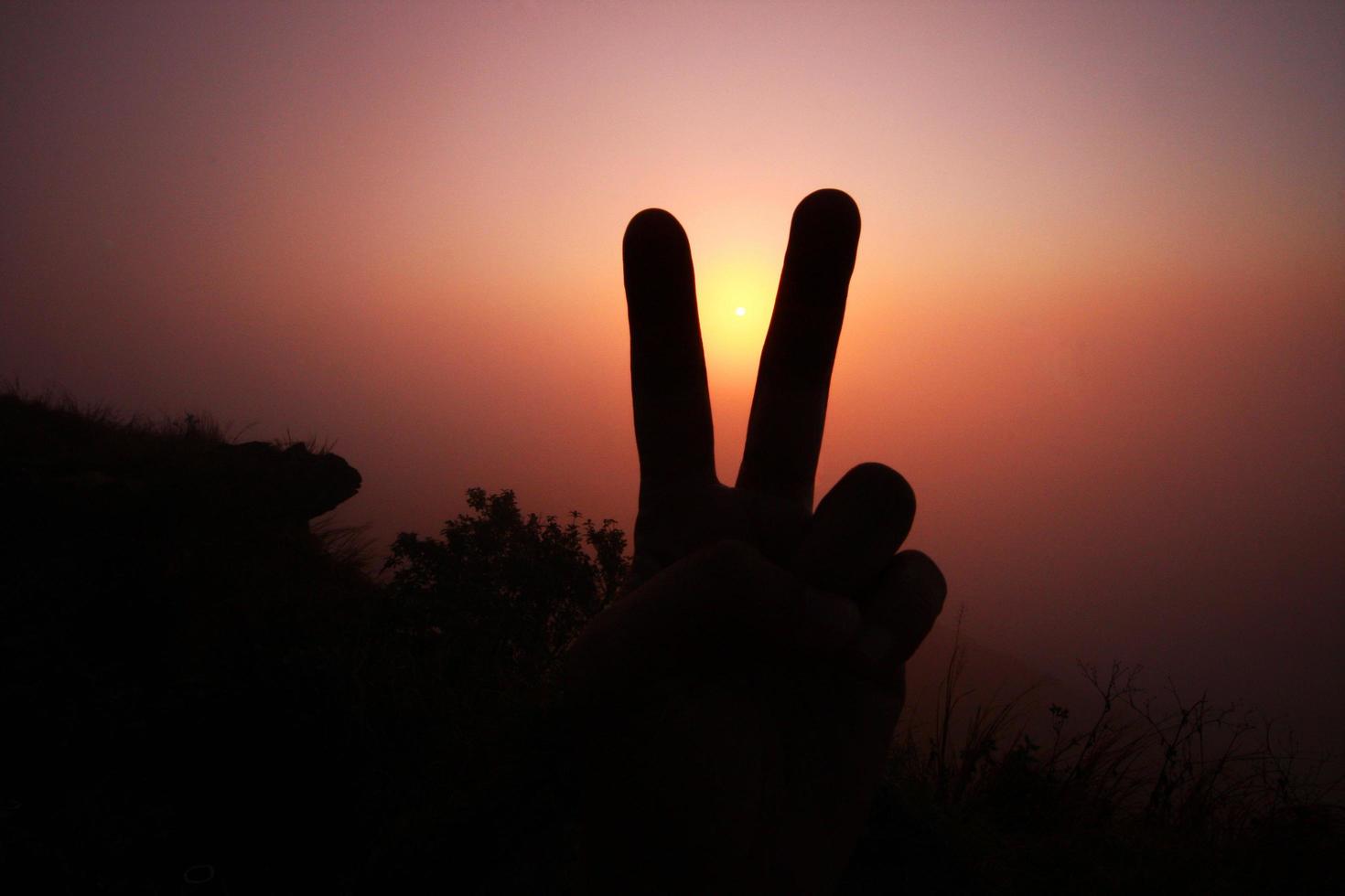 Beautiful silhouette of fingers and hand with valley of mountain in foggy and mist of sunrise shining on the sky photo