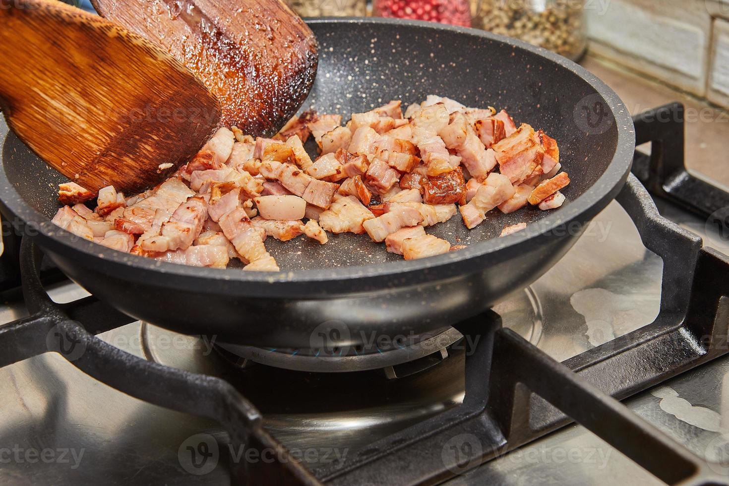 Chopped bacon with onions is fried in pan on gas stove photo